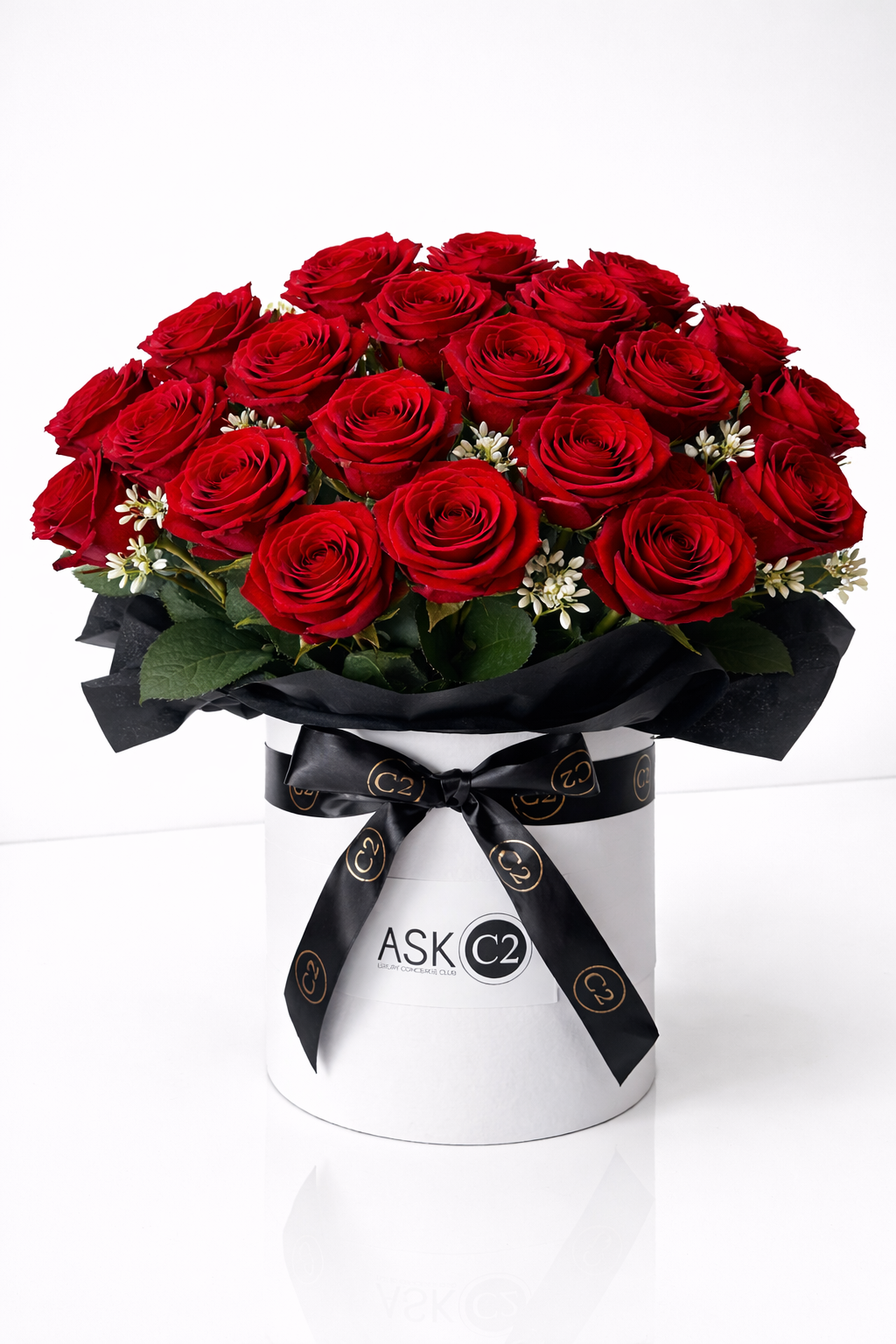 Bouquet of red roses with small white flowers in a white box wrapped with black ribbon labeled 'ASK C2' on a white background.