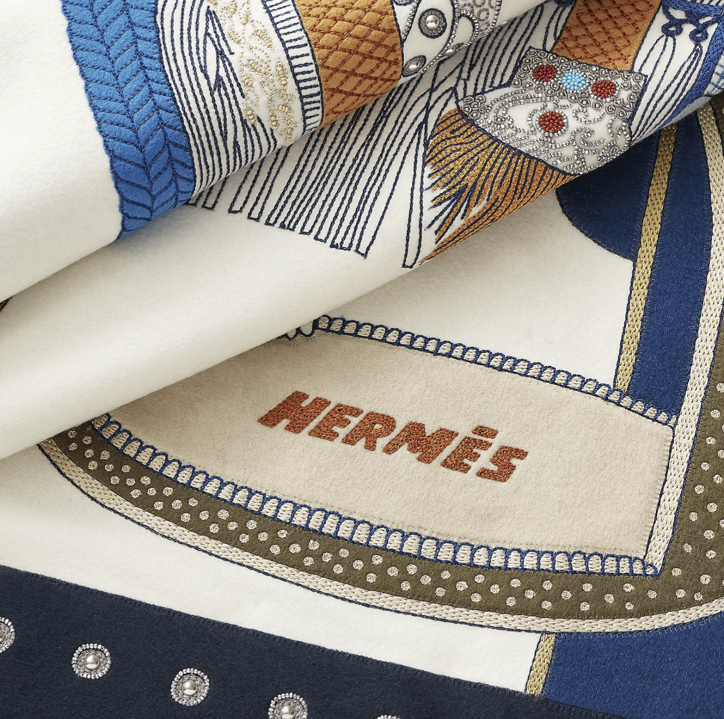 Close-up of embroidered fabric with the Hermès logo, featuring intricate patterns, detailed stitching, and metallic embellishments.