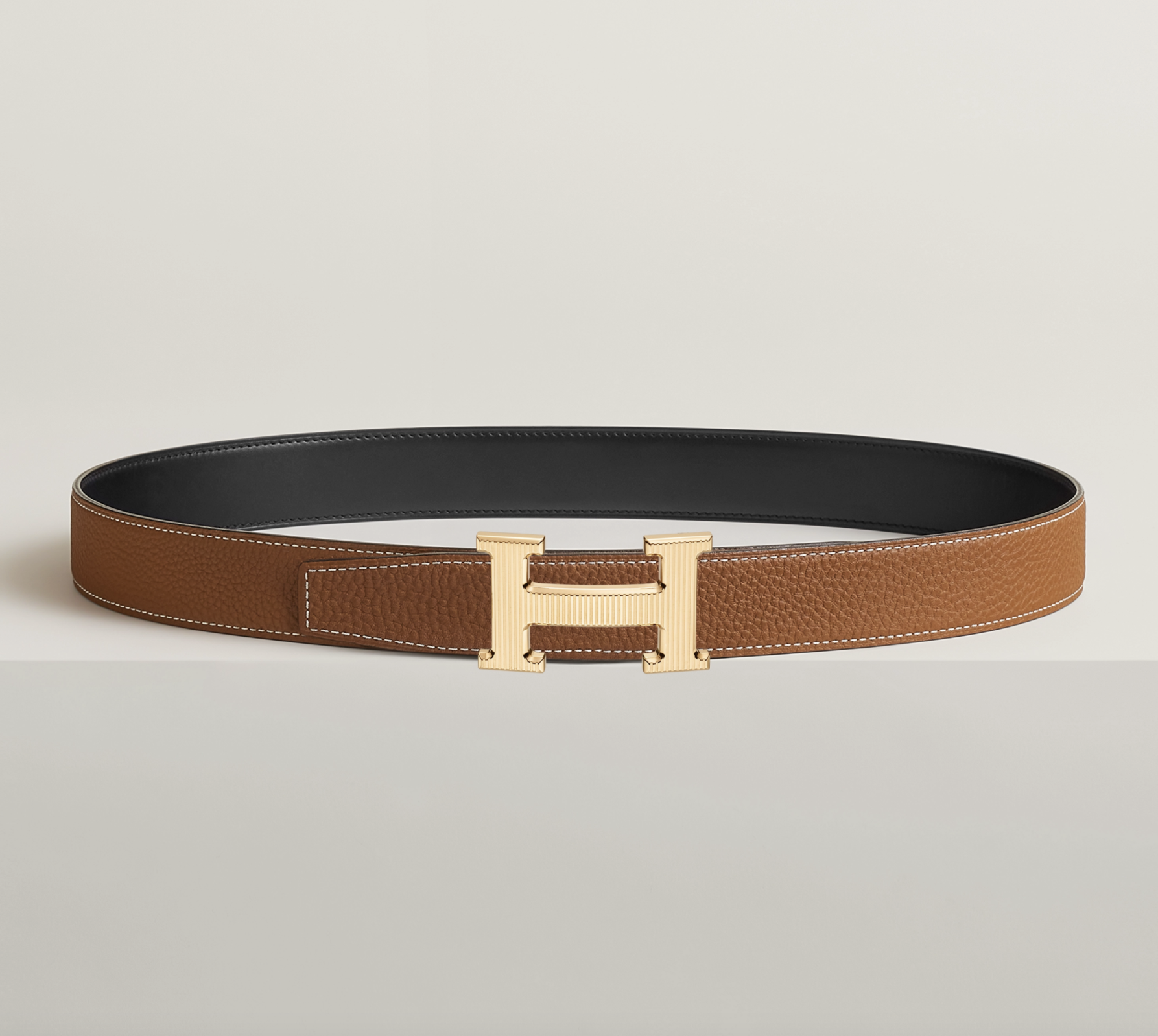 Brown leather belt with a large gold 'H' buckle on a plain white background.