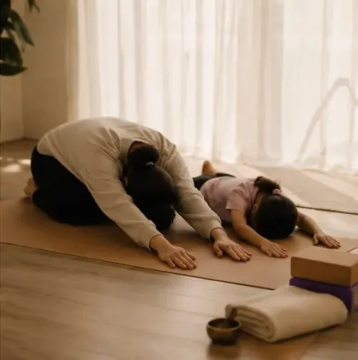 Two people practicing yoga in a room with sunlight, in child's pose on mats.
