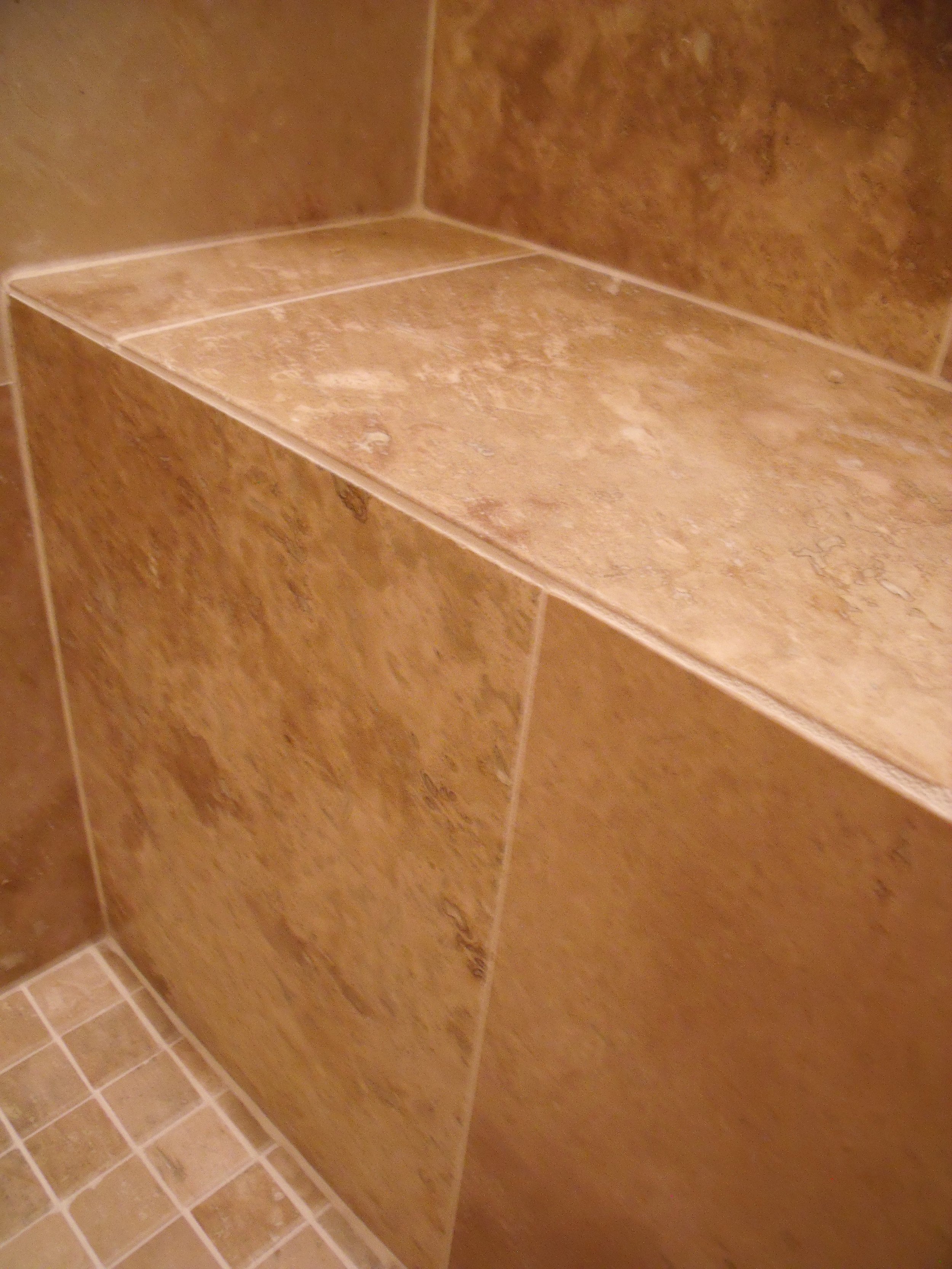 Close-up view of brown tiled wall and floor with a built-in tiled shelf in a bathroom shower.
