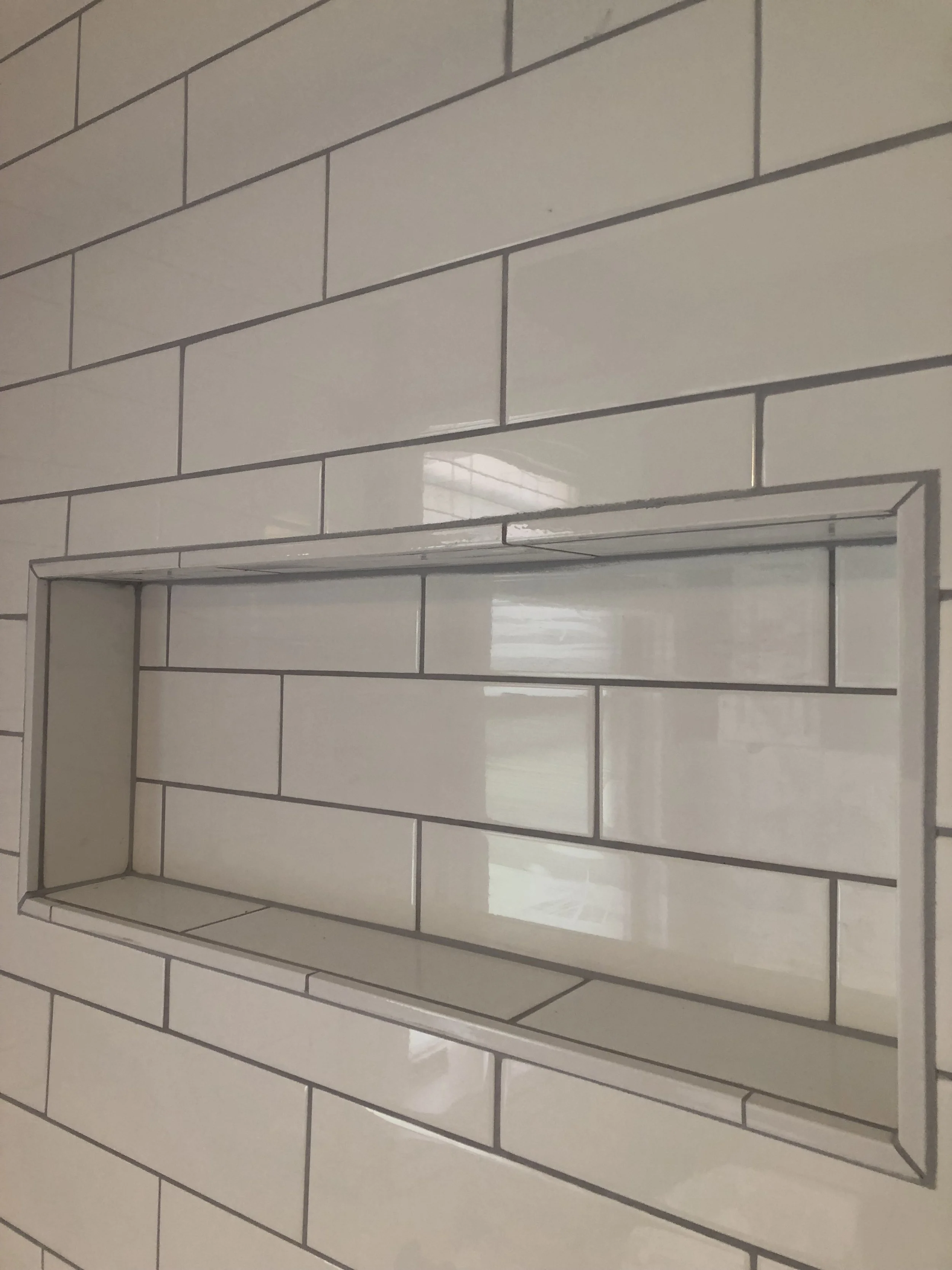 White rectangular tiles on a wall with a recessed shelf outlined by a metal frame.
