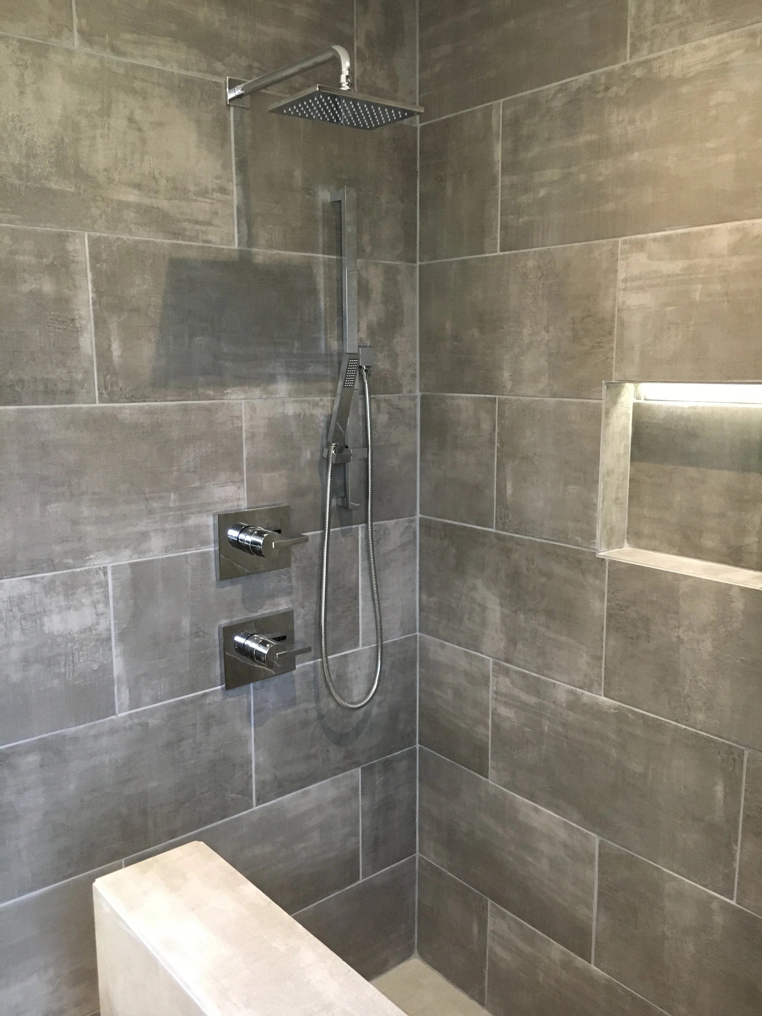 Modern shower with large rain showerhead, handheld shower head, and built-in wall niche in tiled shower area.