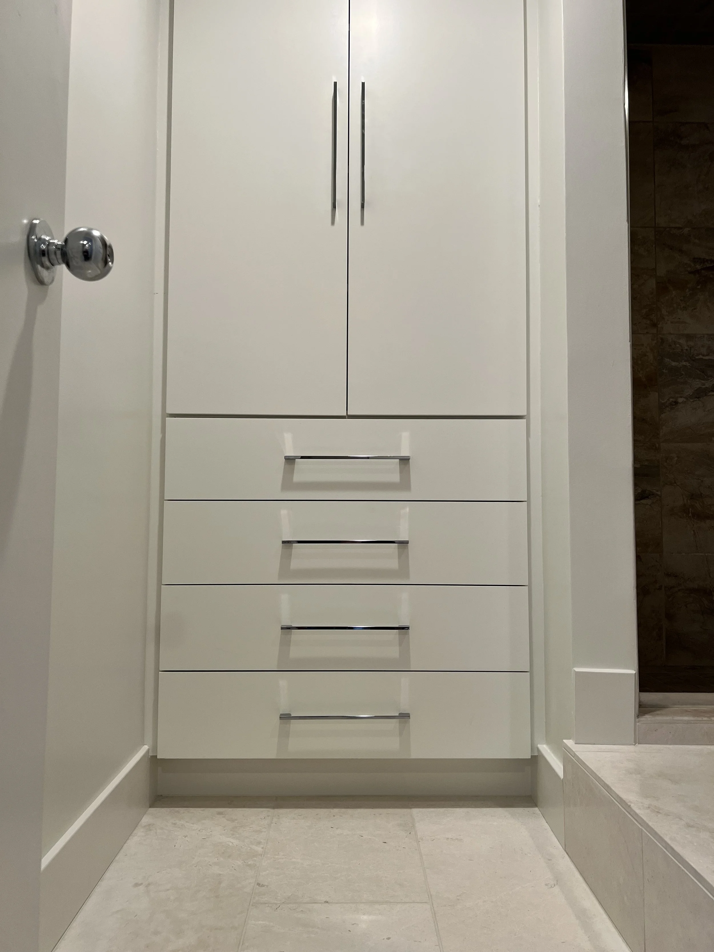 White storage cabinet with two doors on top and four drawers below in a bathroom.