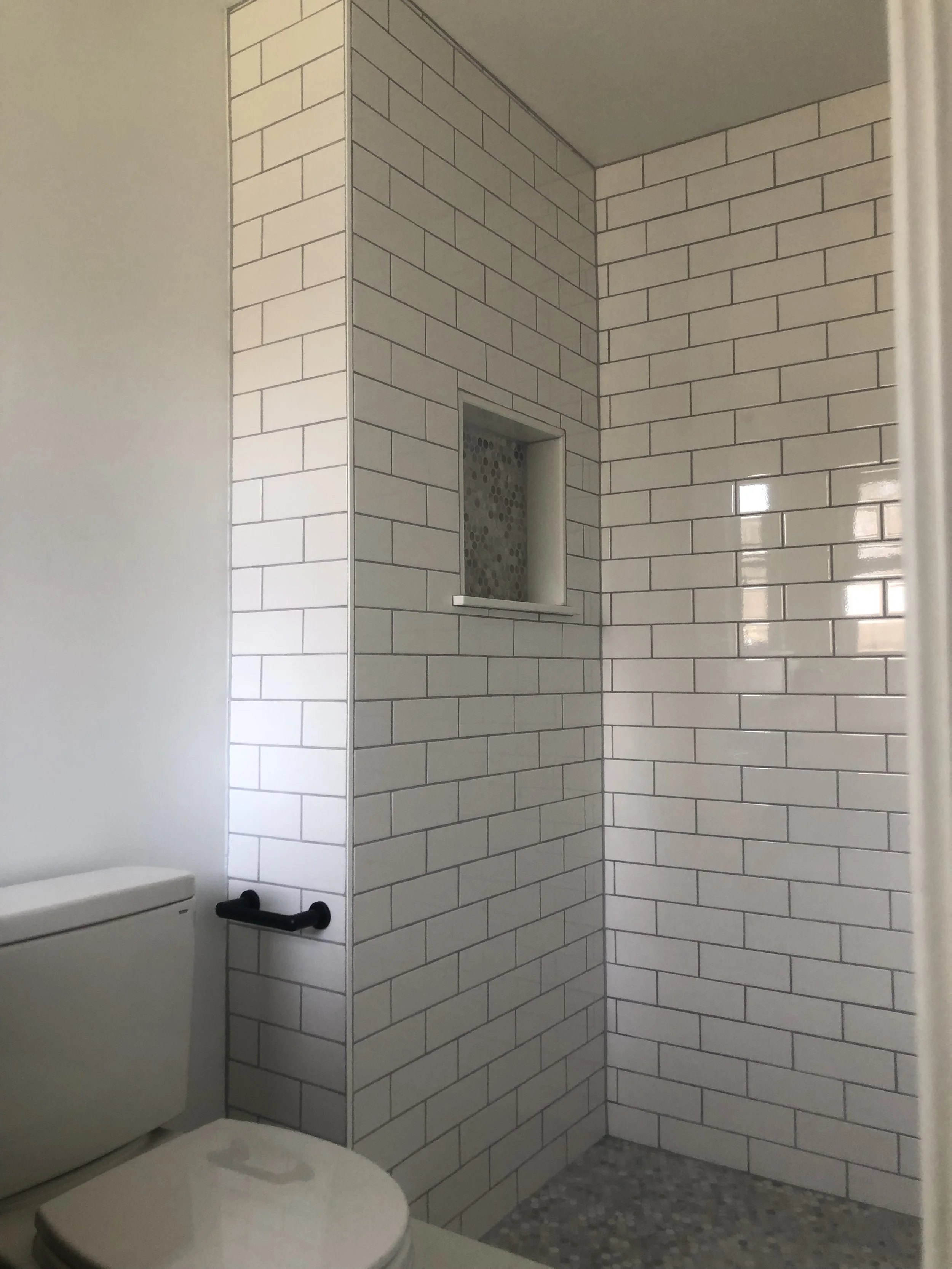 Bathroom with white brick-tiled shower area, built-in niche, corner display, and toilet.