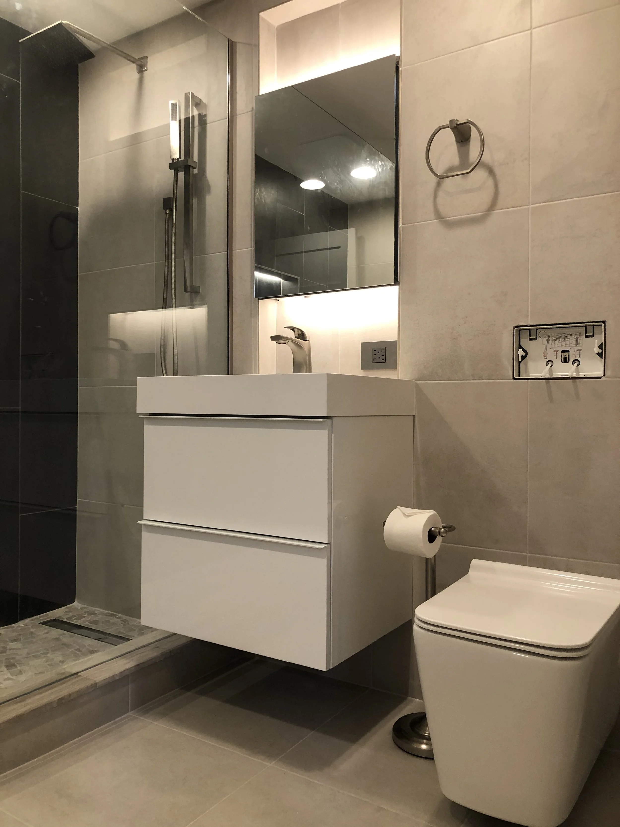 Modern bathroom with a shower, a white floating vanity with a sink, a mirror, a wall-mounted towel ring, and a wall-mounted toilet paper holder with a roll of toilet paper.