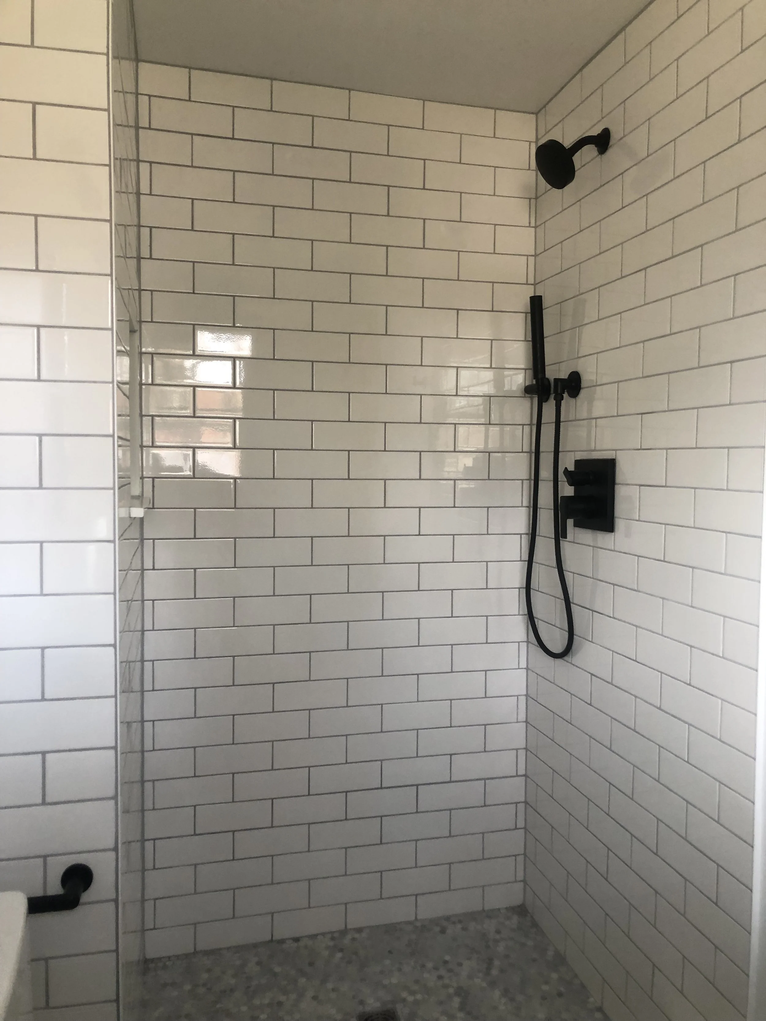 A modern shower with white subway tile walls, black shower fixtures, and a pebble stone floor.