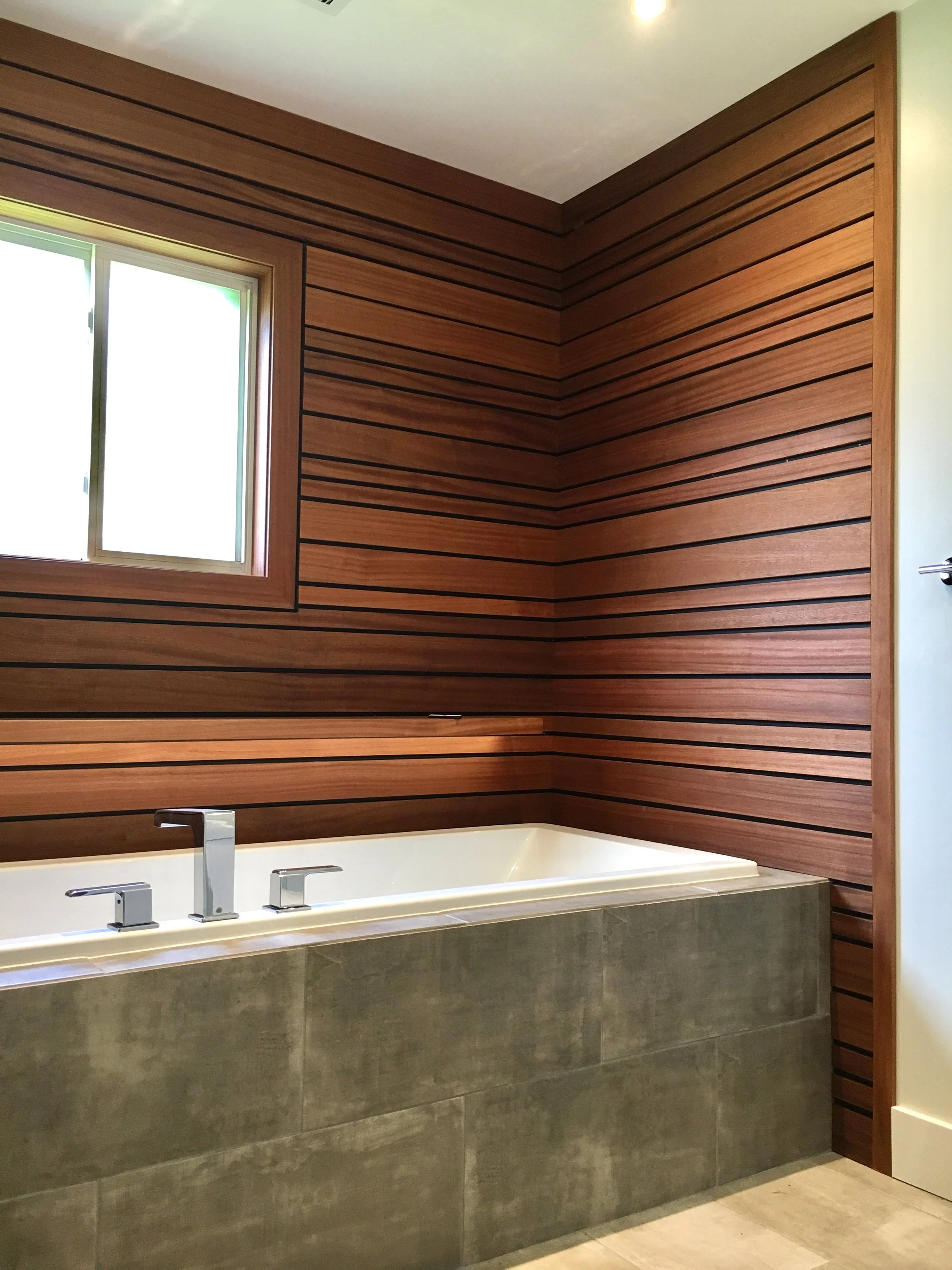 Modern bathroom with wood-paneled walls, a large bathtub with a concrete exterior, a window, and a chrome faucet.
