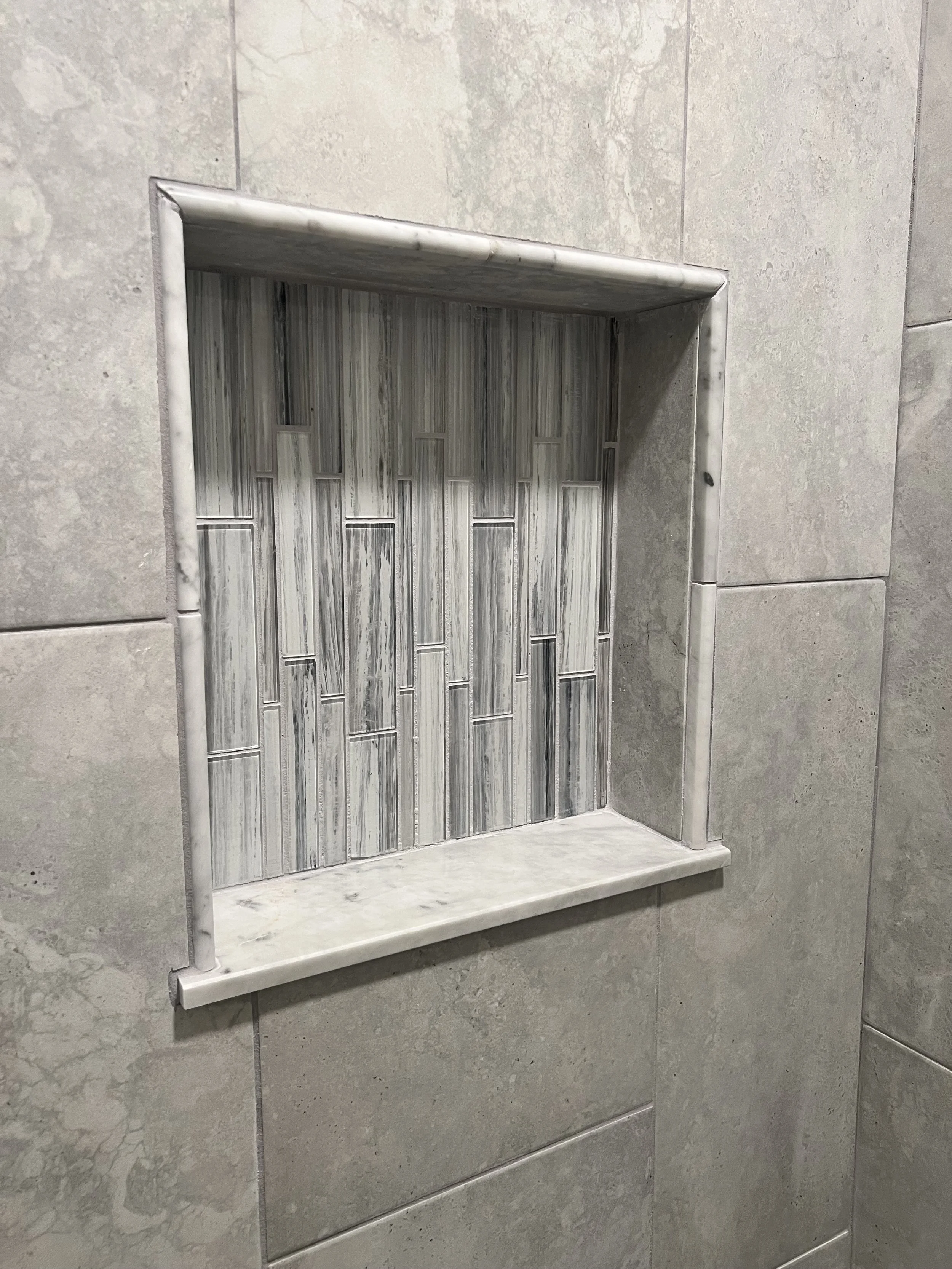 Decorative tile inset in a tiled wall with gray and white tones, bordered by marble trim.