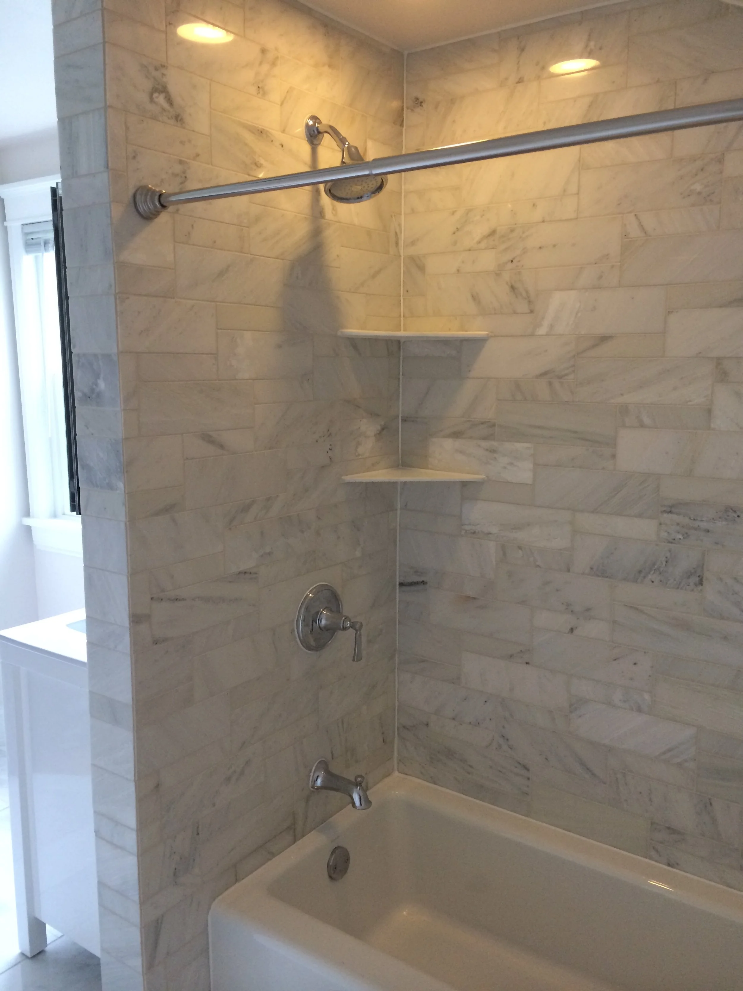 Bathroom shower with marble tiles, a showerhead, a soap dish, and a bathtub.