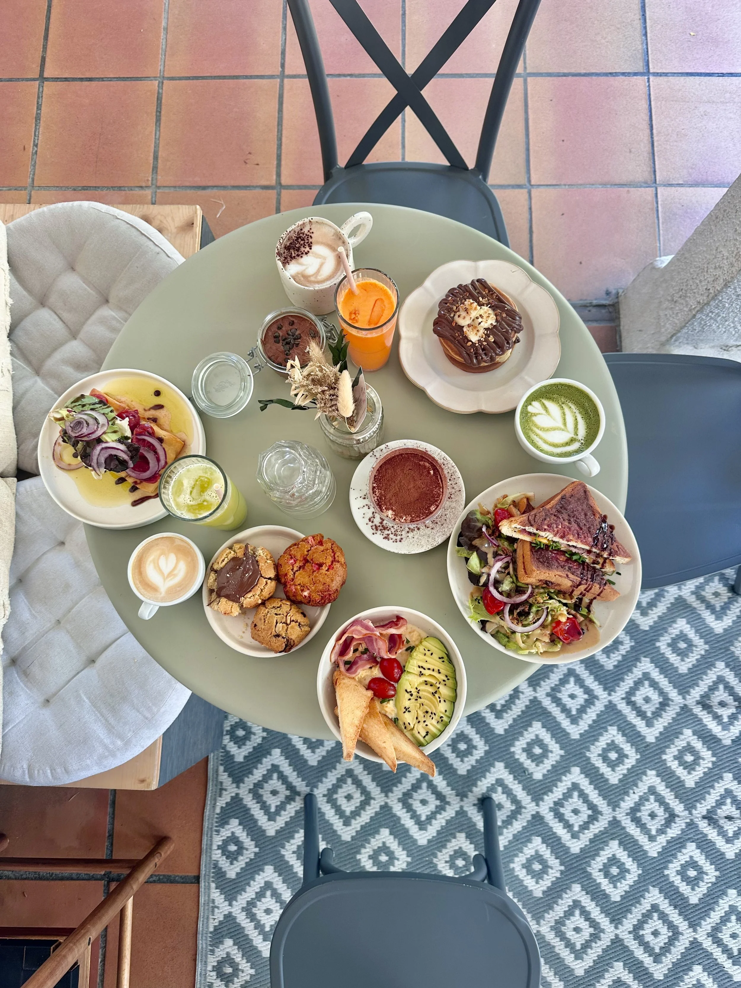 Table ronde avec un petit déjeuner varié comprenant des boissons, pâtisseries, salade, sandwich et fruits, vue de dessus.