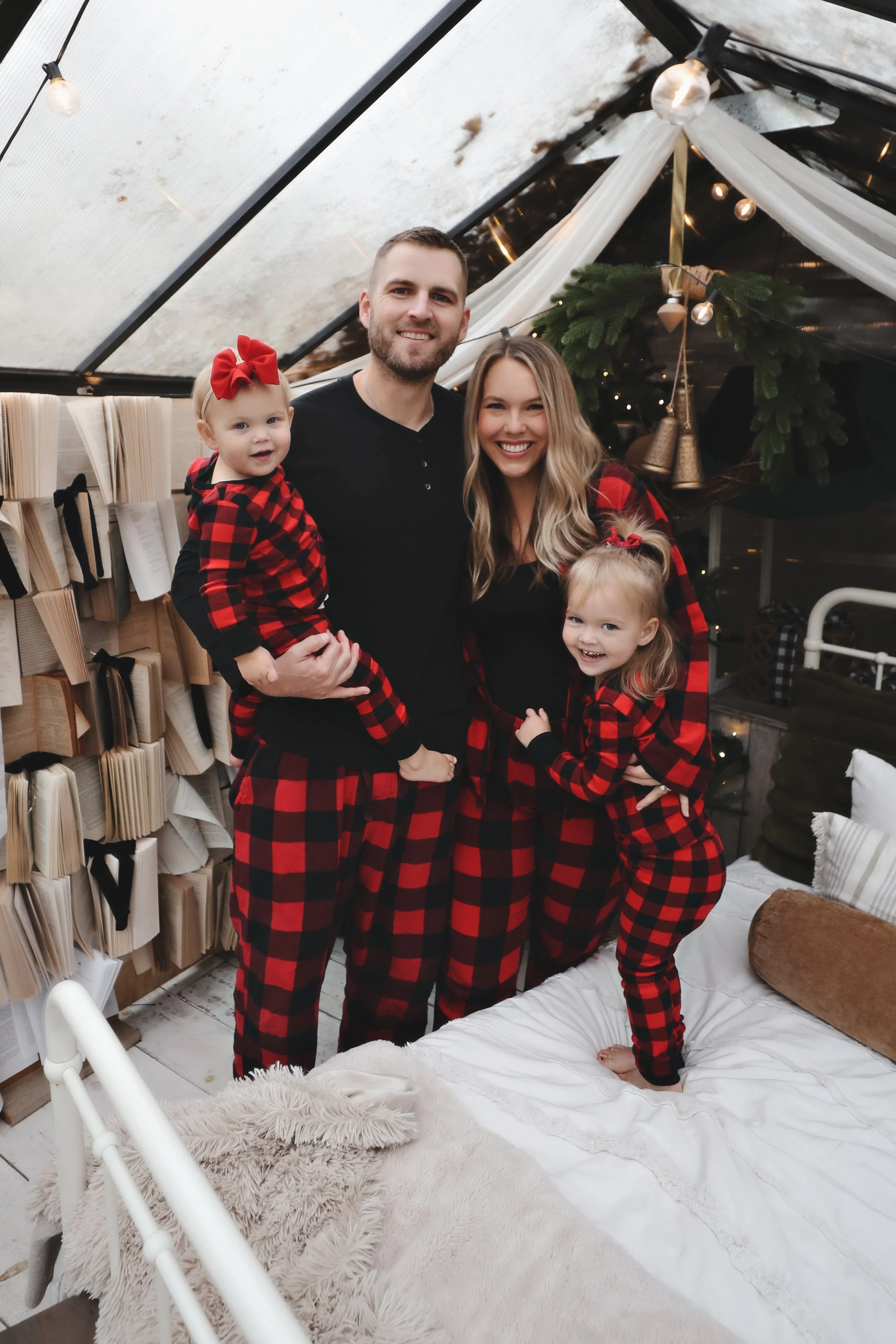 Family of four in matching red and black plaid pajamas inside a decorated tent, celebrating Christmas.