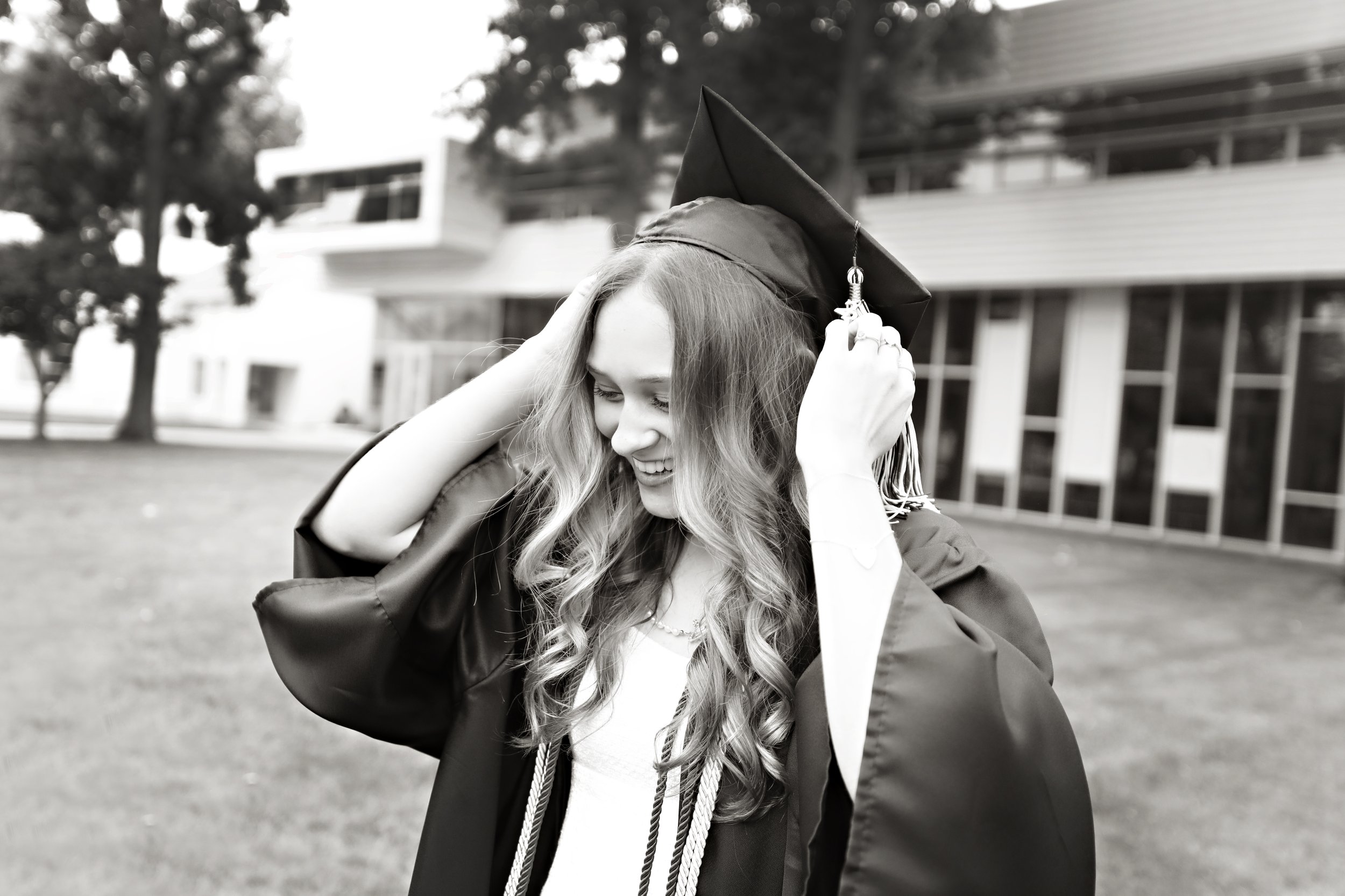 Young woman in graduation gown and cap adjusting her cap outdoors.