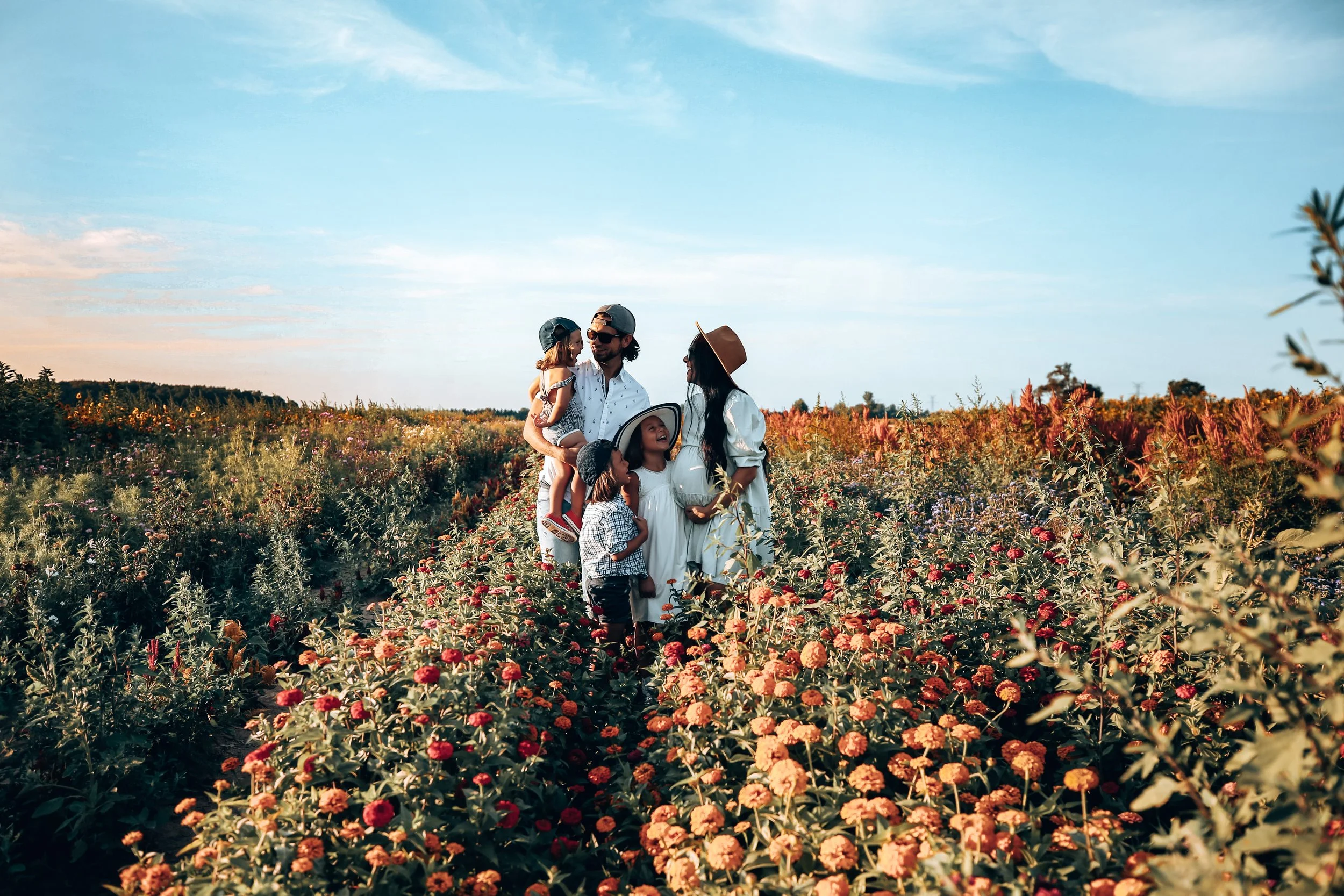 A family of six standing in a colorful field of flowers under a blue sky, with adults and children enjoying the outdoors.