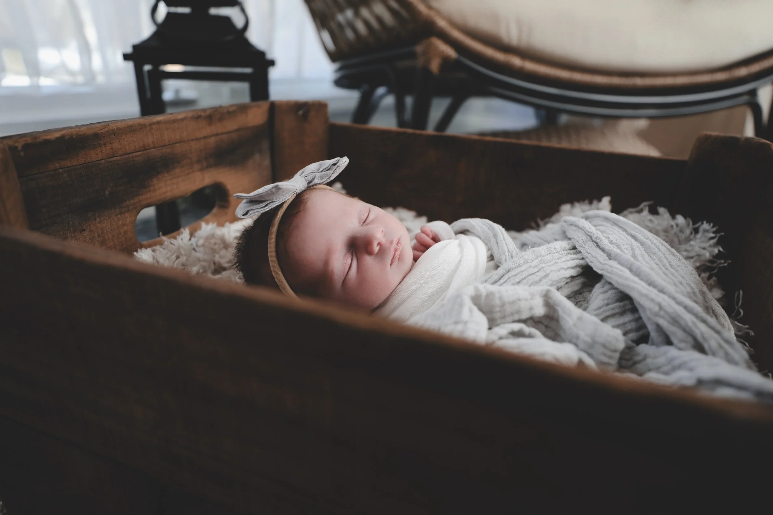 A sleeping baby lying in a wooden cradle with a soft blanket and a headband with a bow.