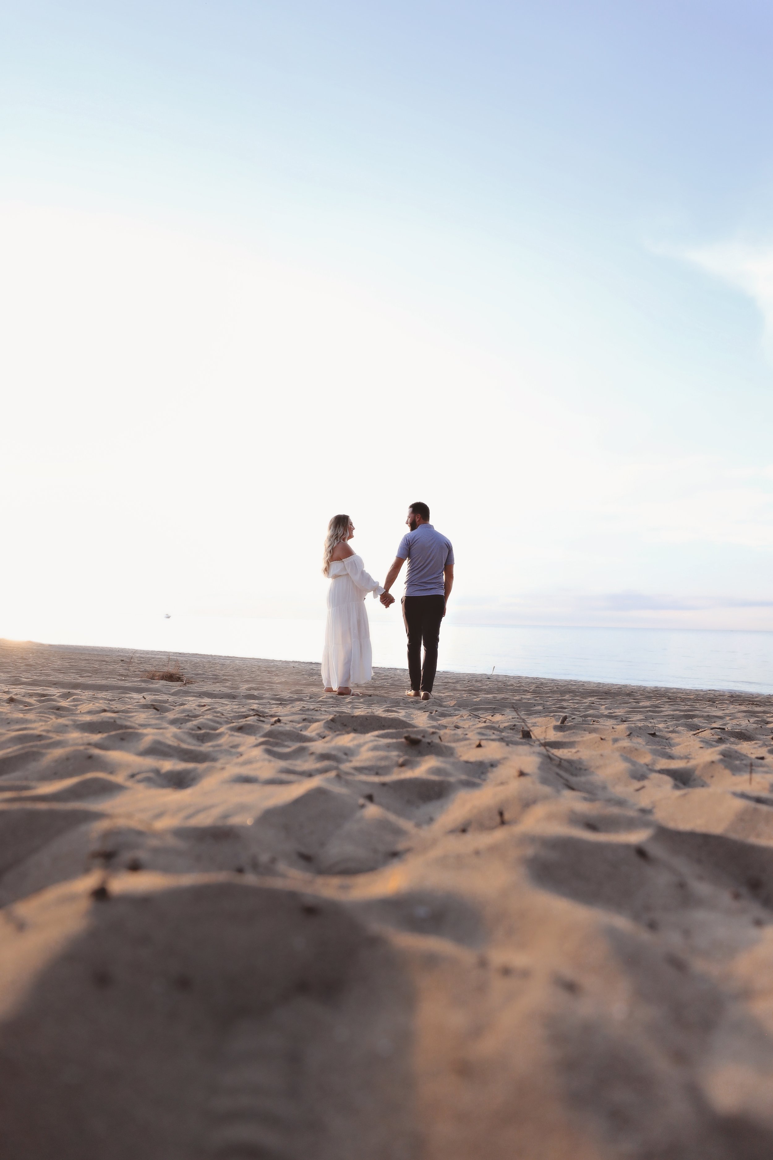 A couple holding hands and walking on a sandy beach during sunset.