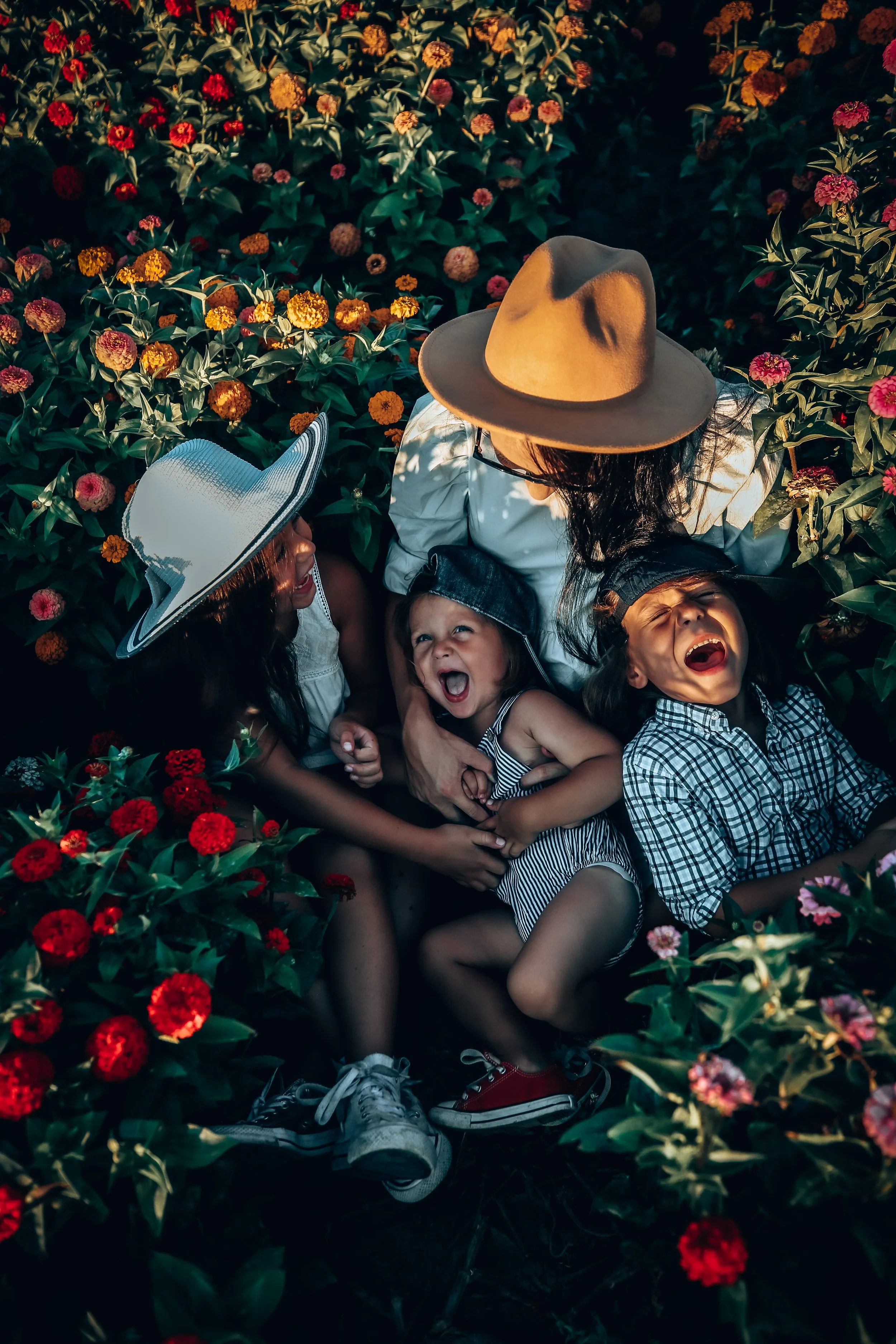 A woman and three children laughing and playing among colorful flowers in a garden.