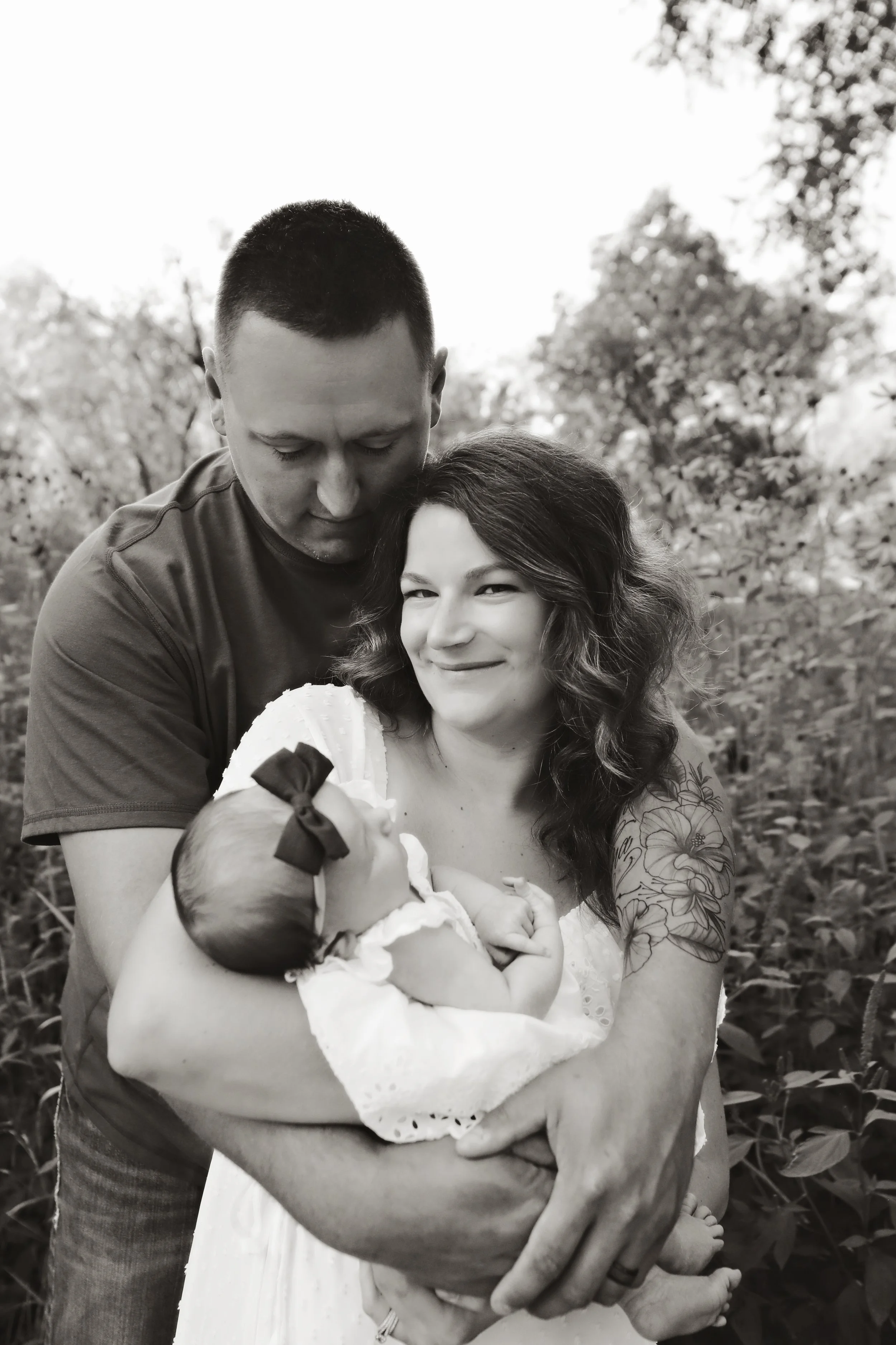 A couple holding their newborn baby in an outdoor setting, black and white photo.