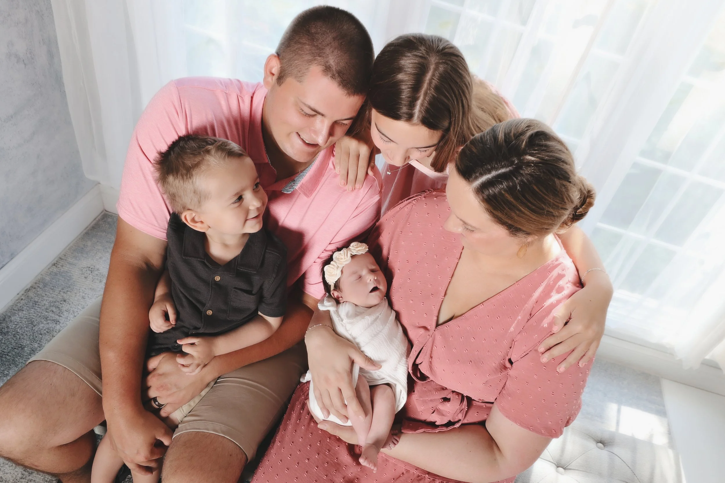 Family gathered around a newborn, family members smiling and looking at the baby.