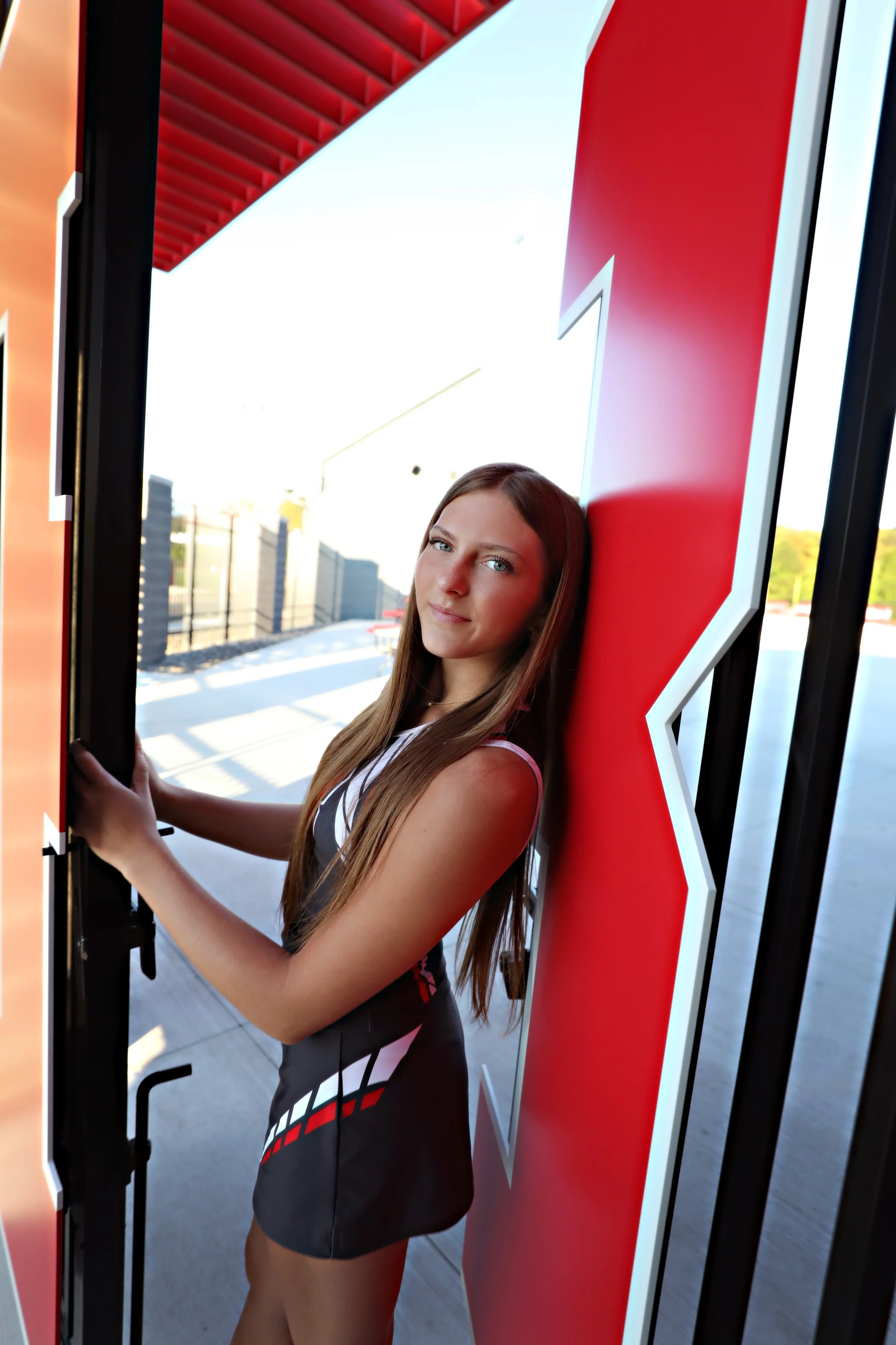 A young woman with long brown hair looking at the camera while standing next to a large red and white 'X' sign at a fast-food restaurant.