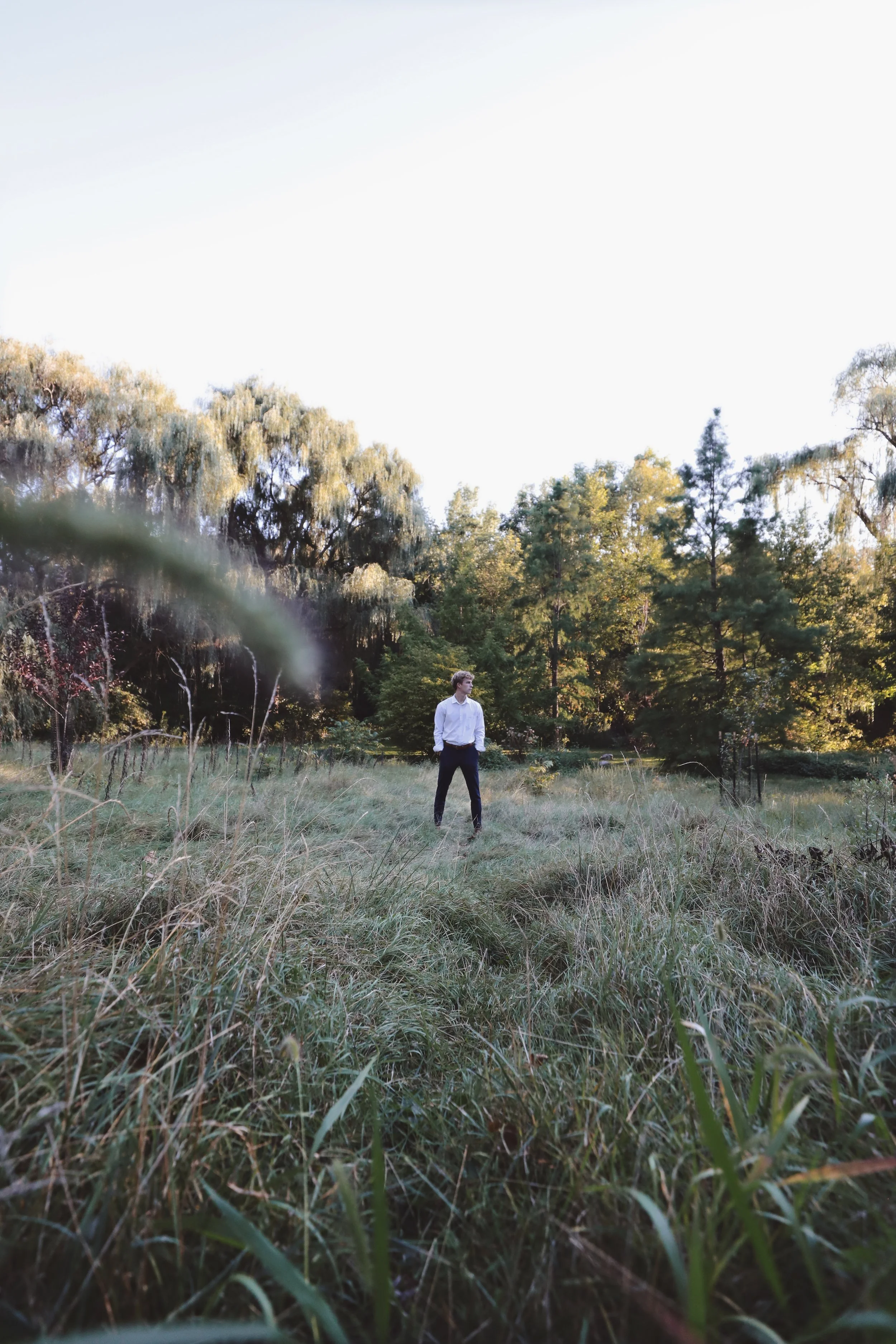 A man standing alone in a grassy field with trees in the background.