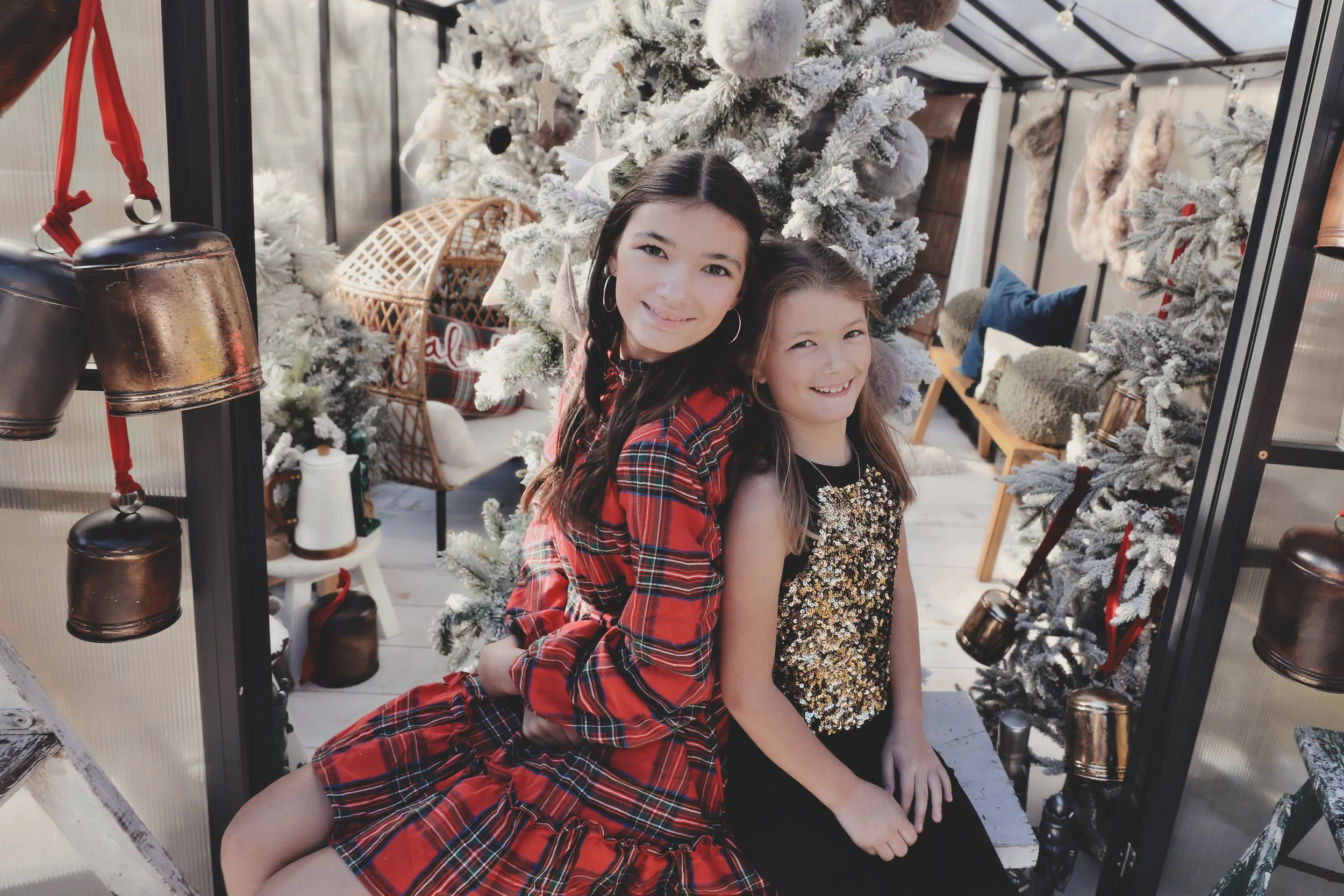 Two girls smiling in front of a decorated Christmas tree, with holiday-themed ornaments and a cozy, festive background.