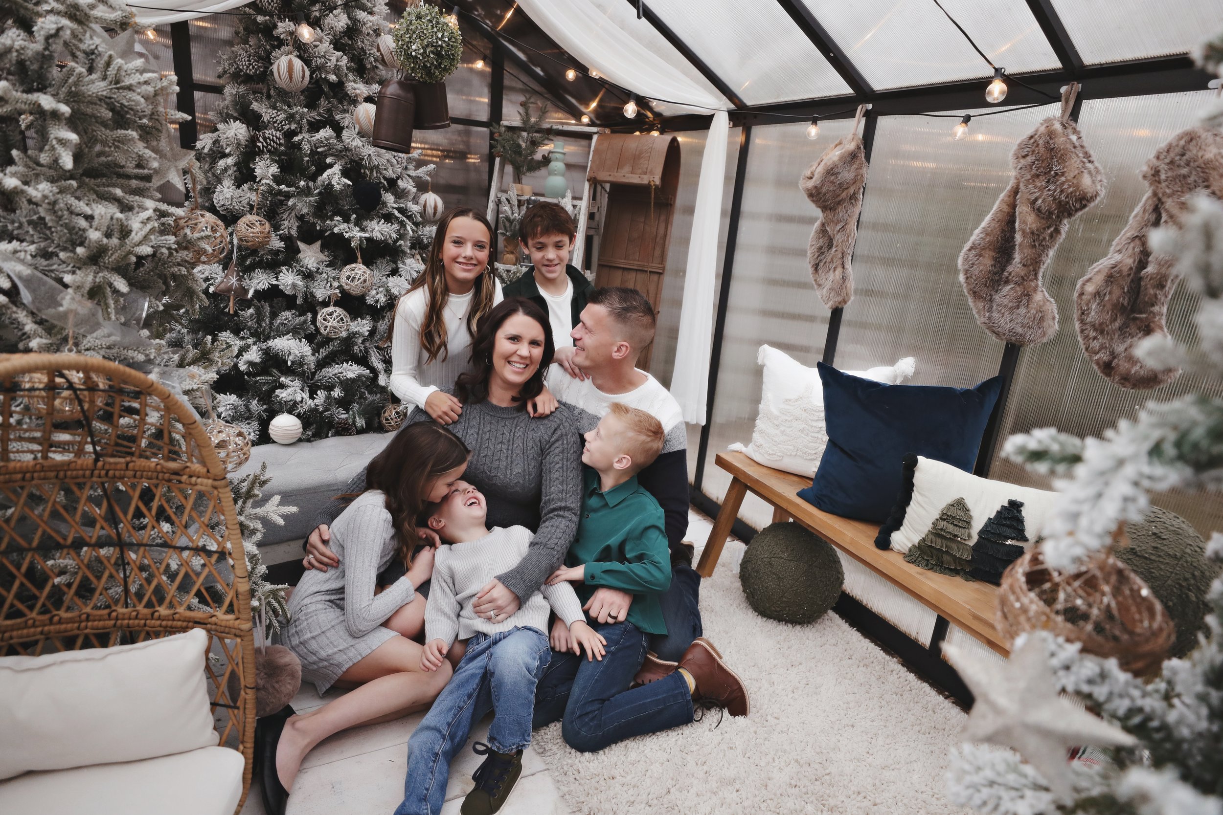 A family of seven celebrating Christmas indoors with a decorated tree, stockings, and cozy decorations.