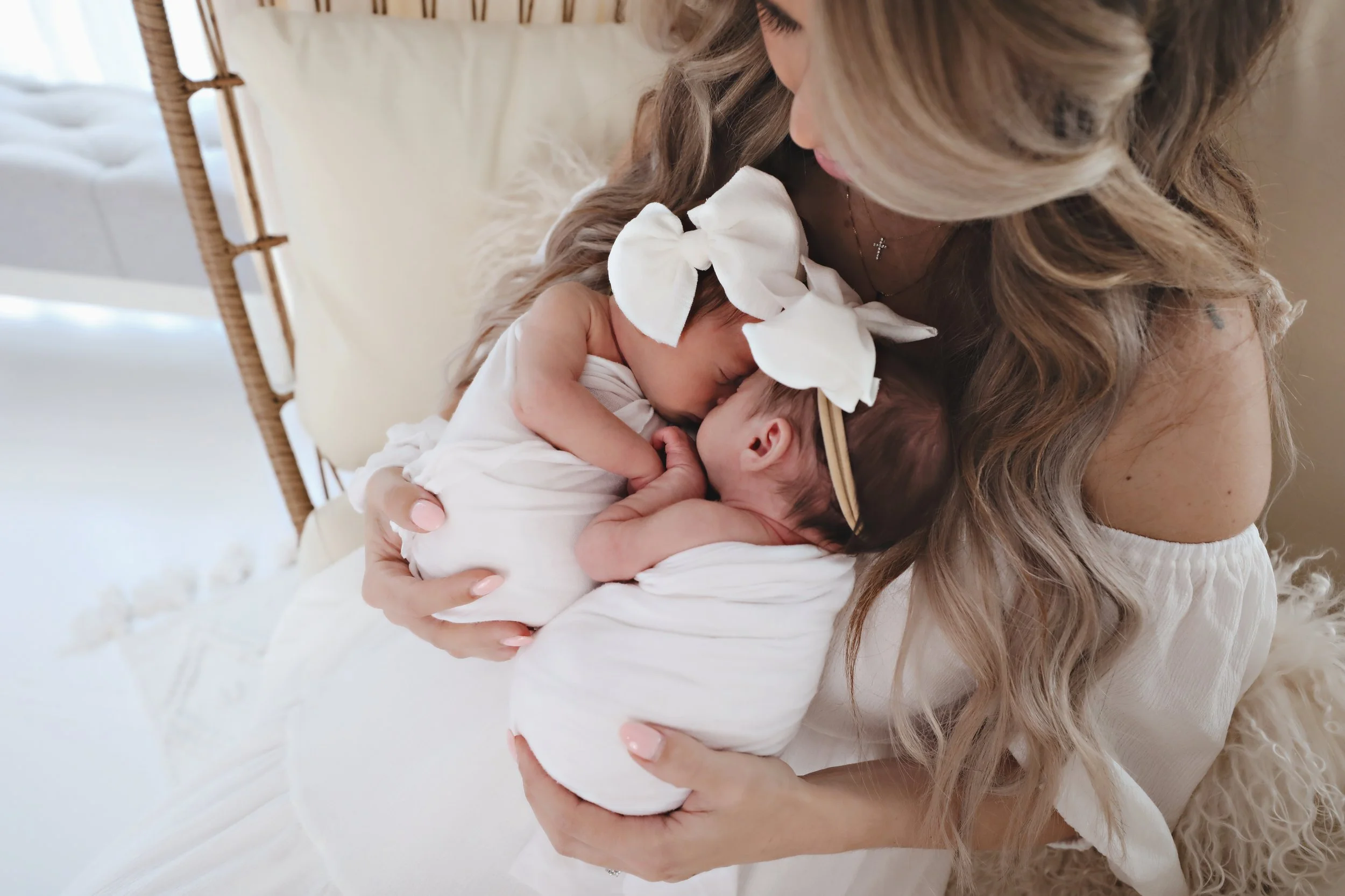 A mother holding two newborn babies close to her chest, sharing a tender moment, in a bright room with soft lighting.