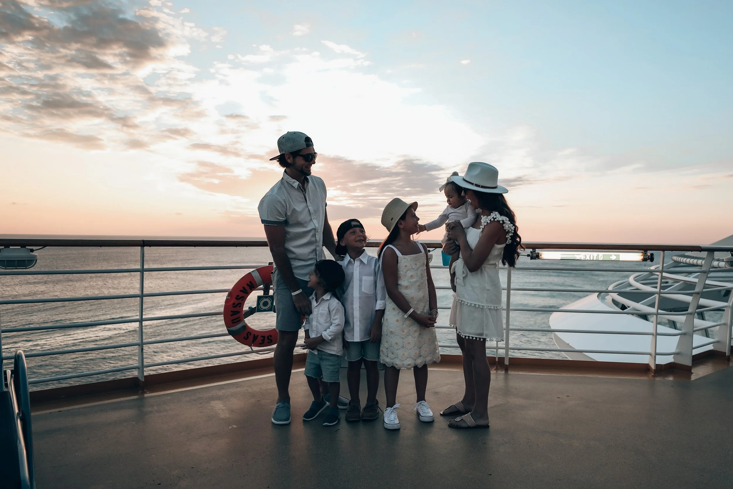 Family enjoying sunset on a cruise ship deck, with ocean and sky in the background.