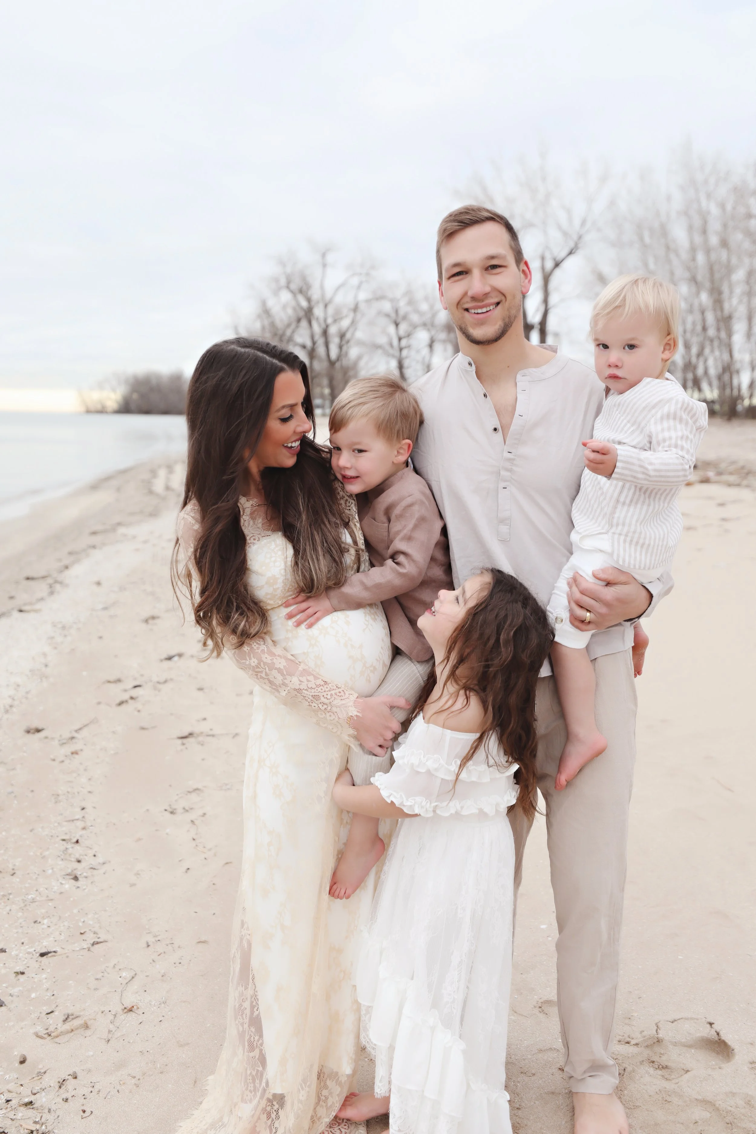 Family of six on a beach, smiling, with leafless trees in the background.