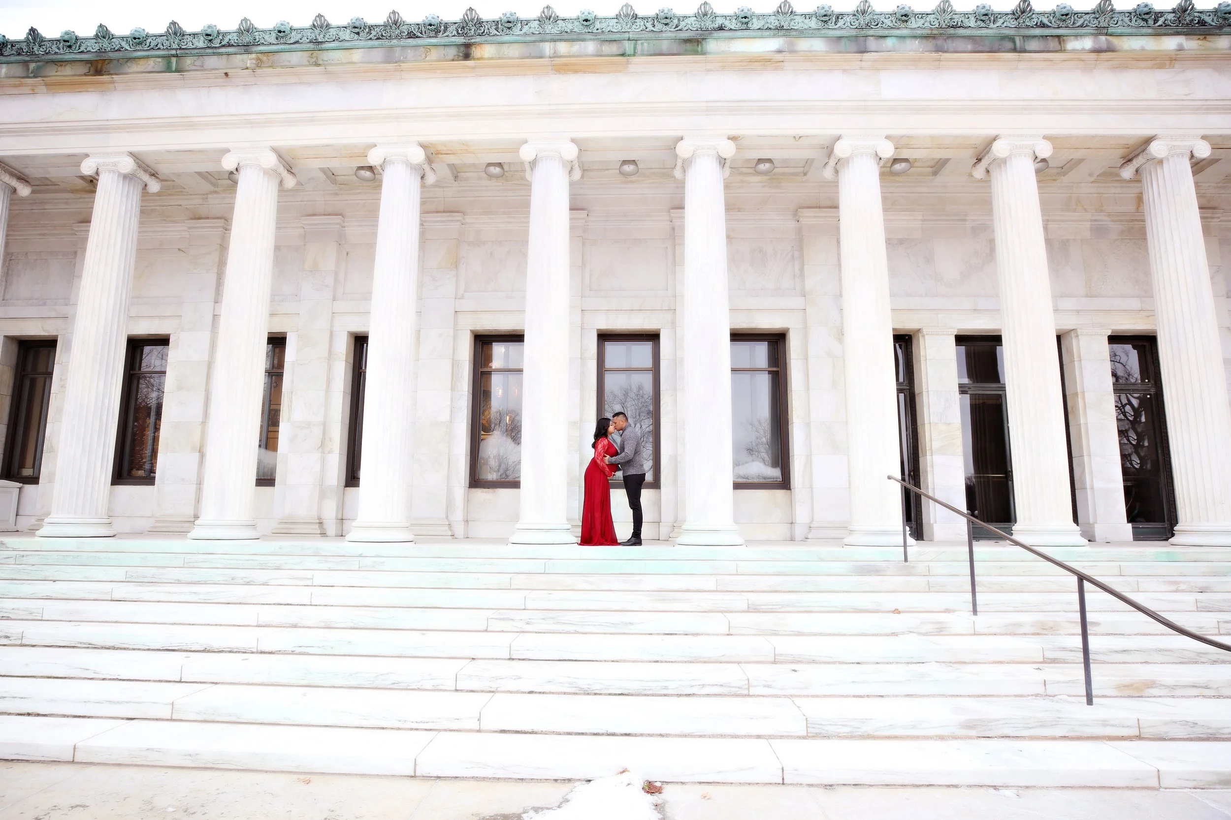 A couple standing closely together and kissing on the steps in front of a building with tall white columns.