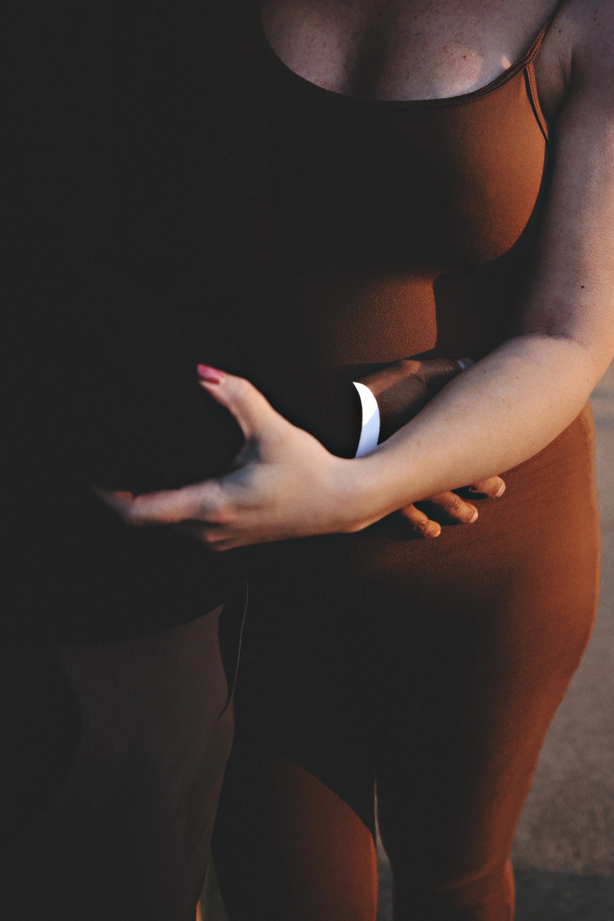 Close-up of a woman in an orange tank top holding a black bag with one hand, standing outdoors.