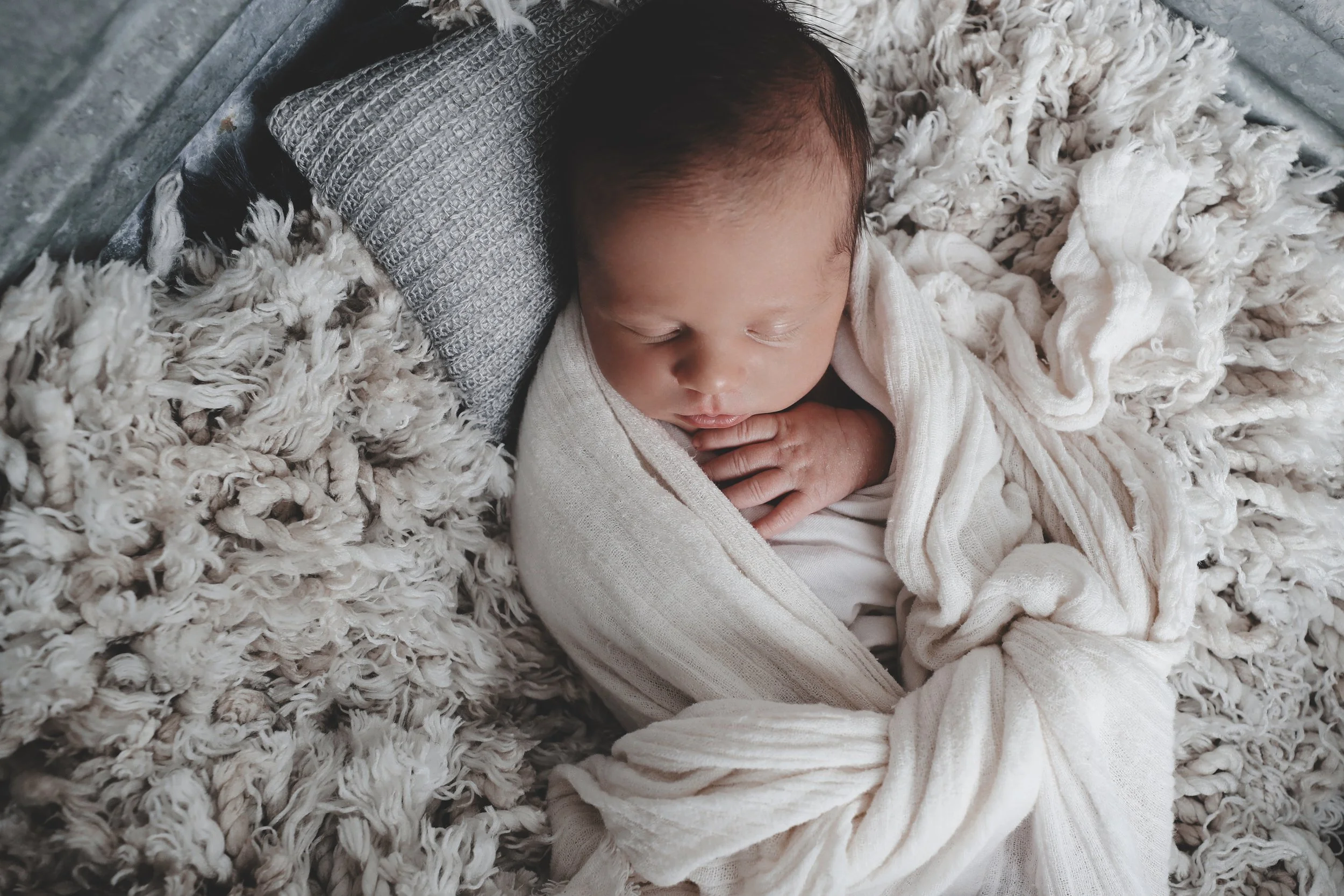 A sleeping baby wrapped in a cream-colored blanket, resting on a soft, textured surface.