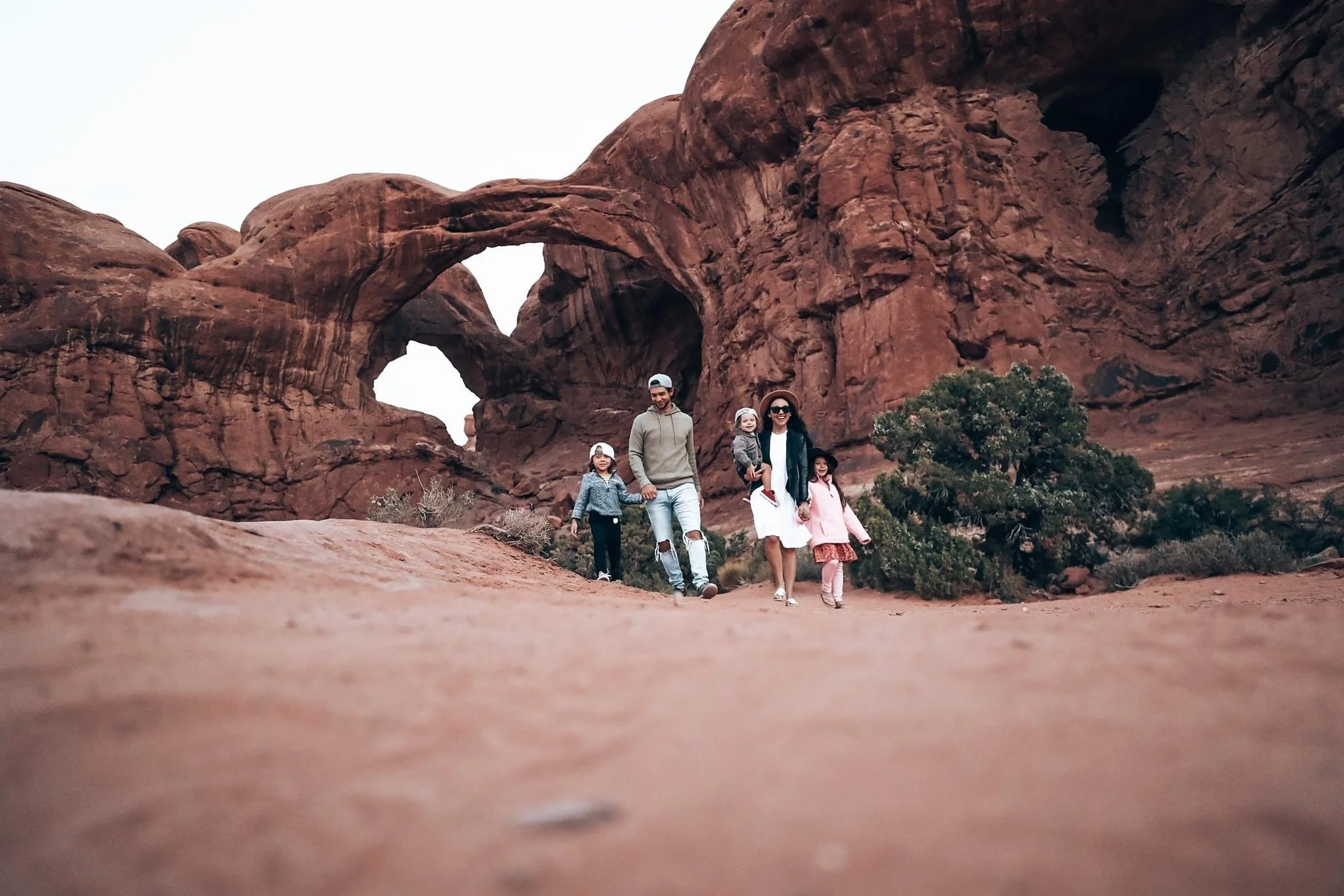 A family of five walking through a desert landscape with large red rock formations and arches in the background.