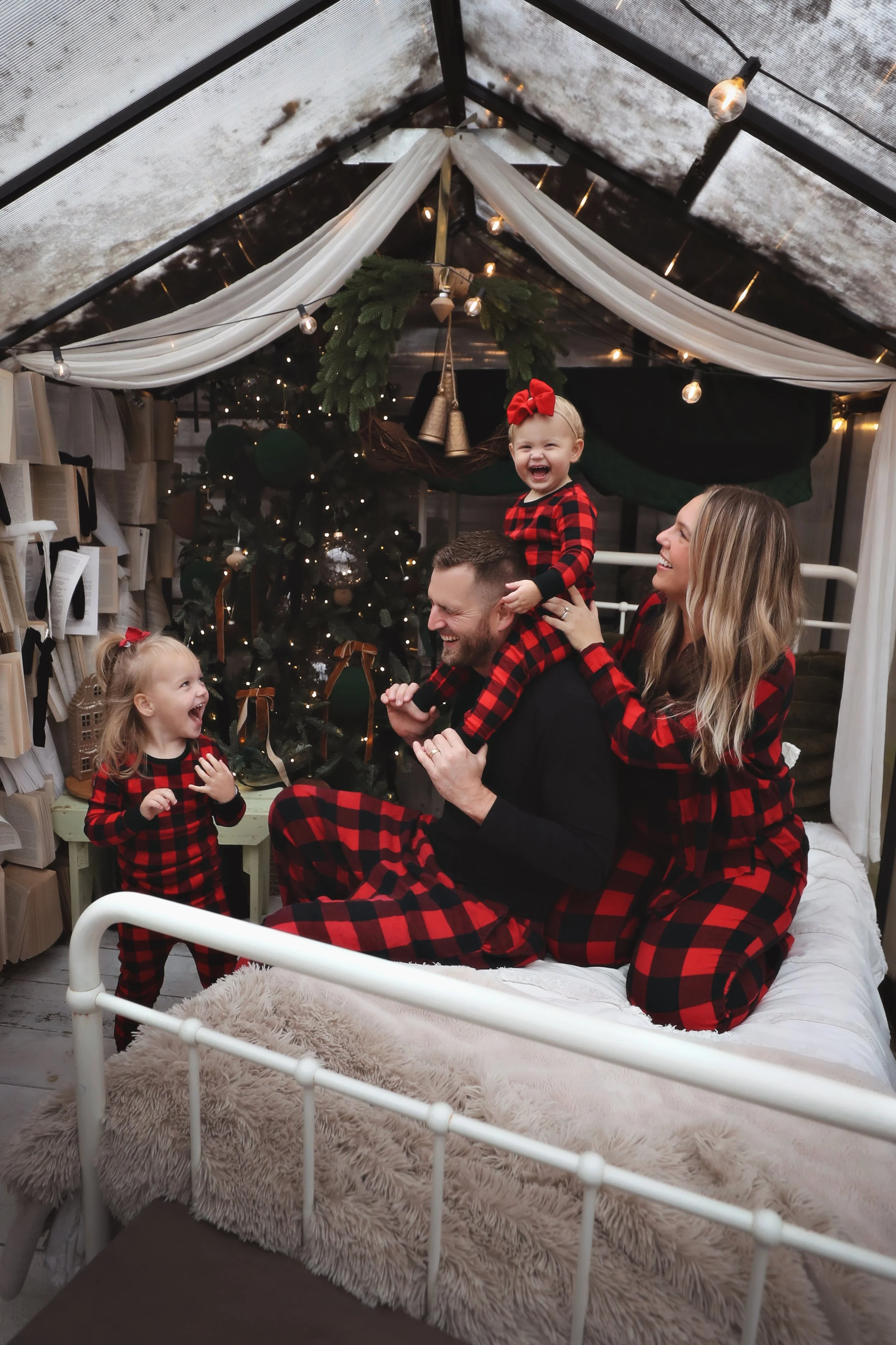 Happy family celebrating Christmas in pajamas near decorated tree, with children wearing red plaid pajamas, inside a cozy, decorated room.