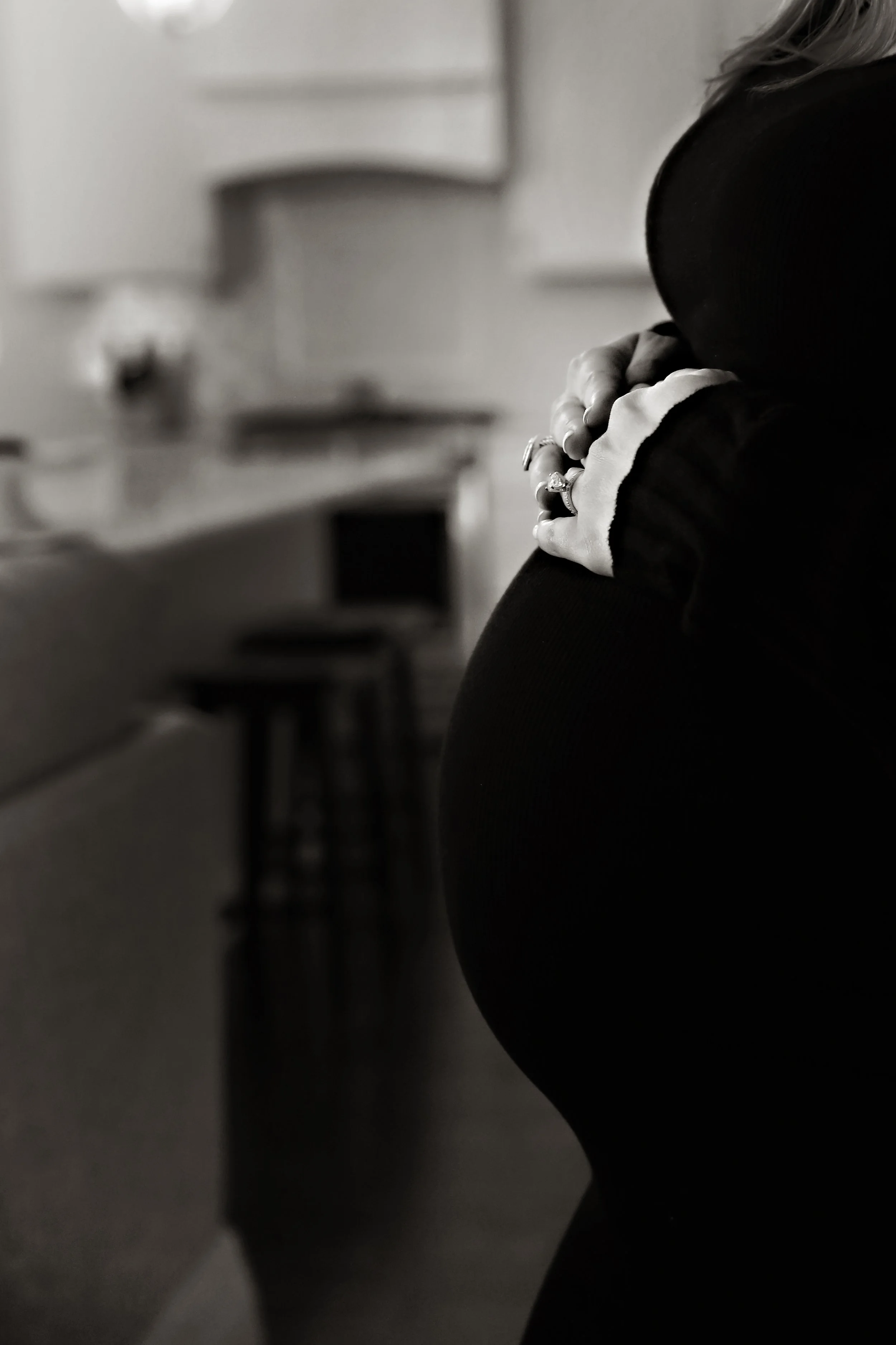Close-up of a person wearing rings and a hoodie, with arms crossed, in a kitchen setting in black and white.