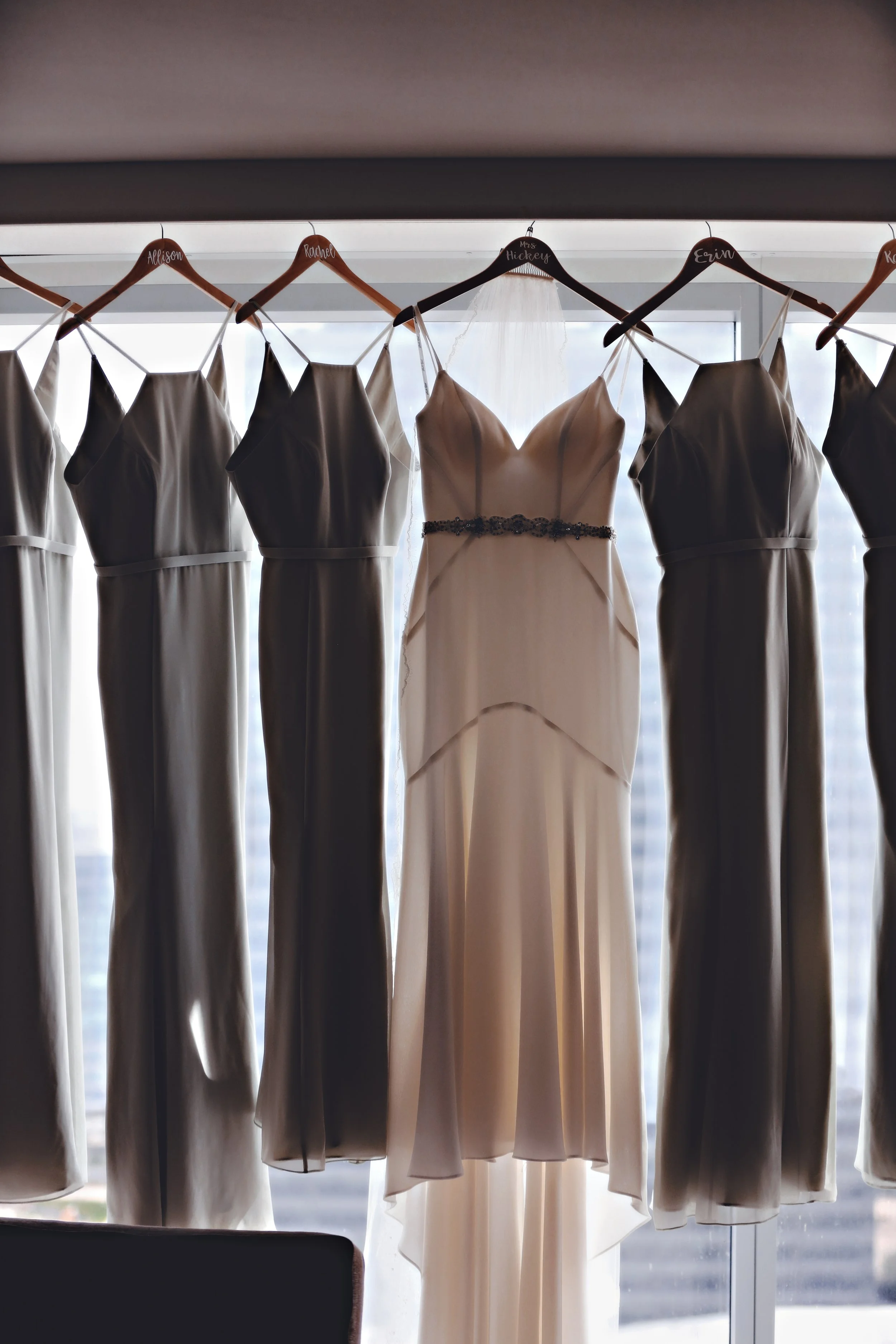Wedding dresses hanging on a rod in front of a window with city buildings visible outside.