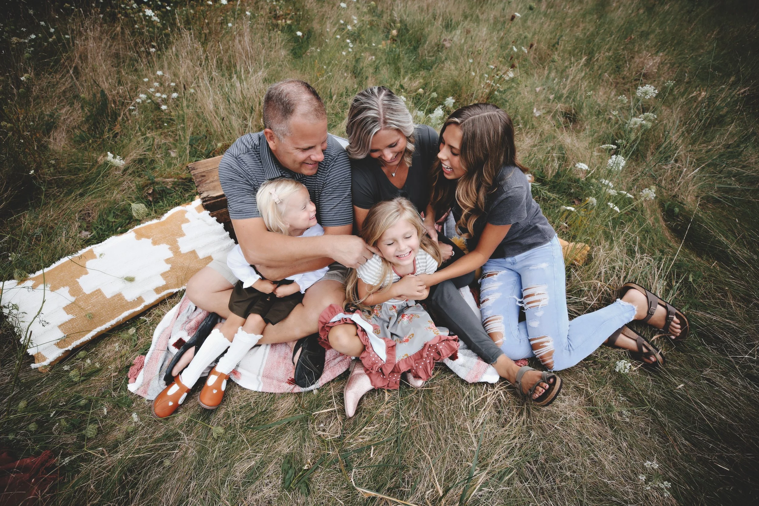 A family of six sitting on a blanket in a grassy field, laughing and playing together.