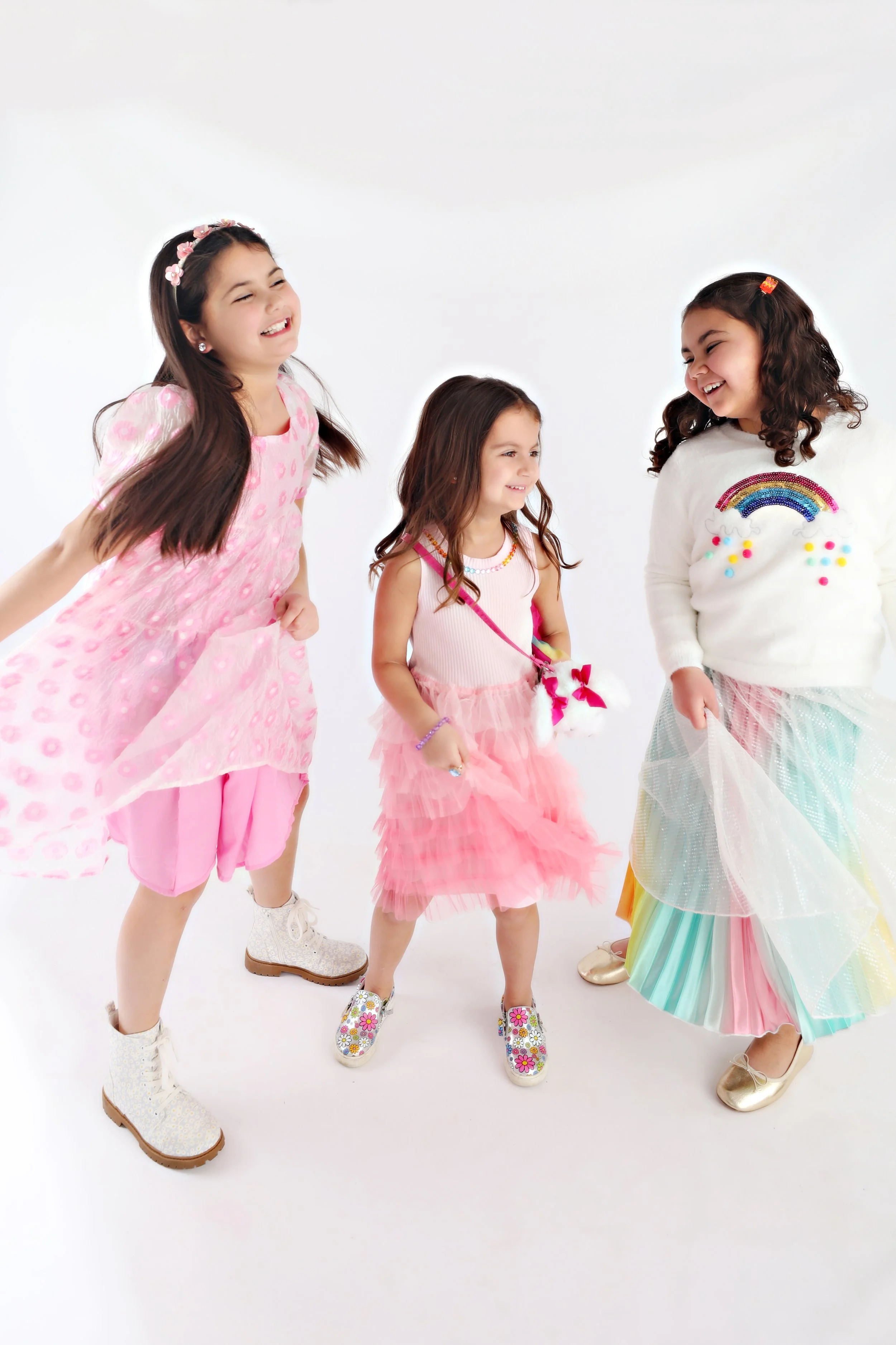 Four young girls in colorful dresses laughing and playing together on a plain white background.