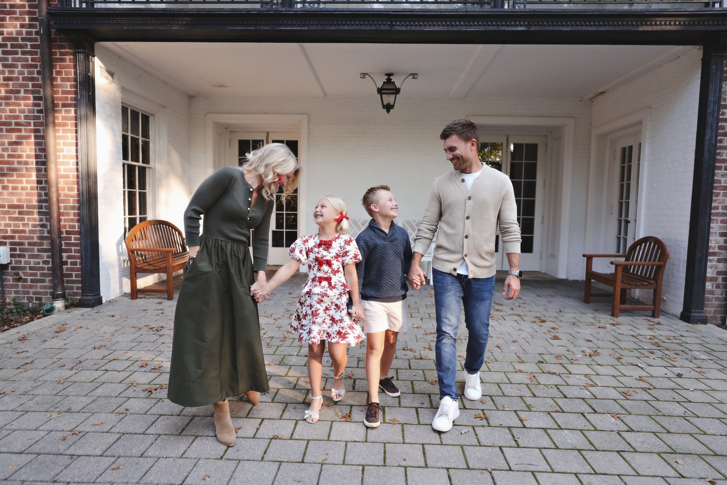 A family of five holding hands and walking together in a driveway outside a house, smiling and looking at each other.