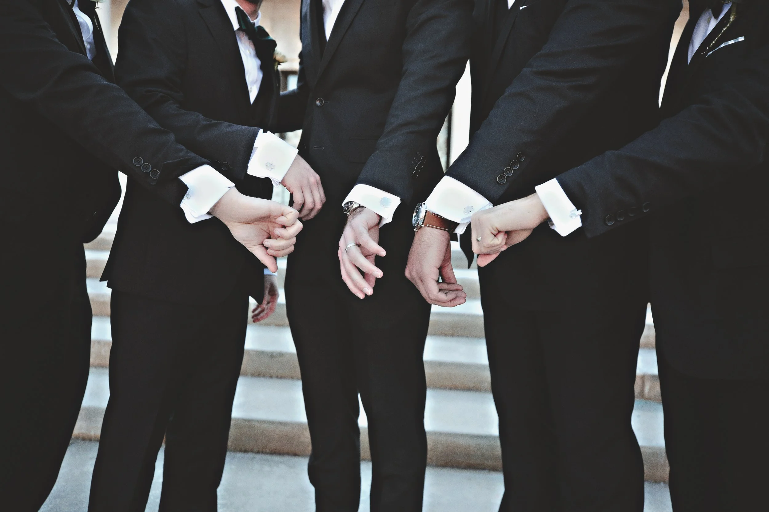 Group of people in formal suits standing in a circle with their fists touching in the middle.