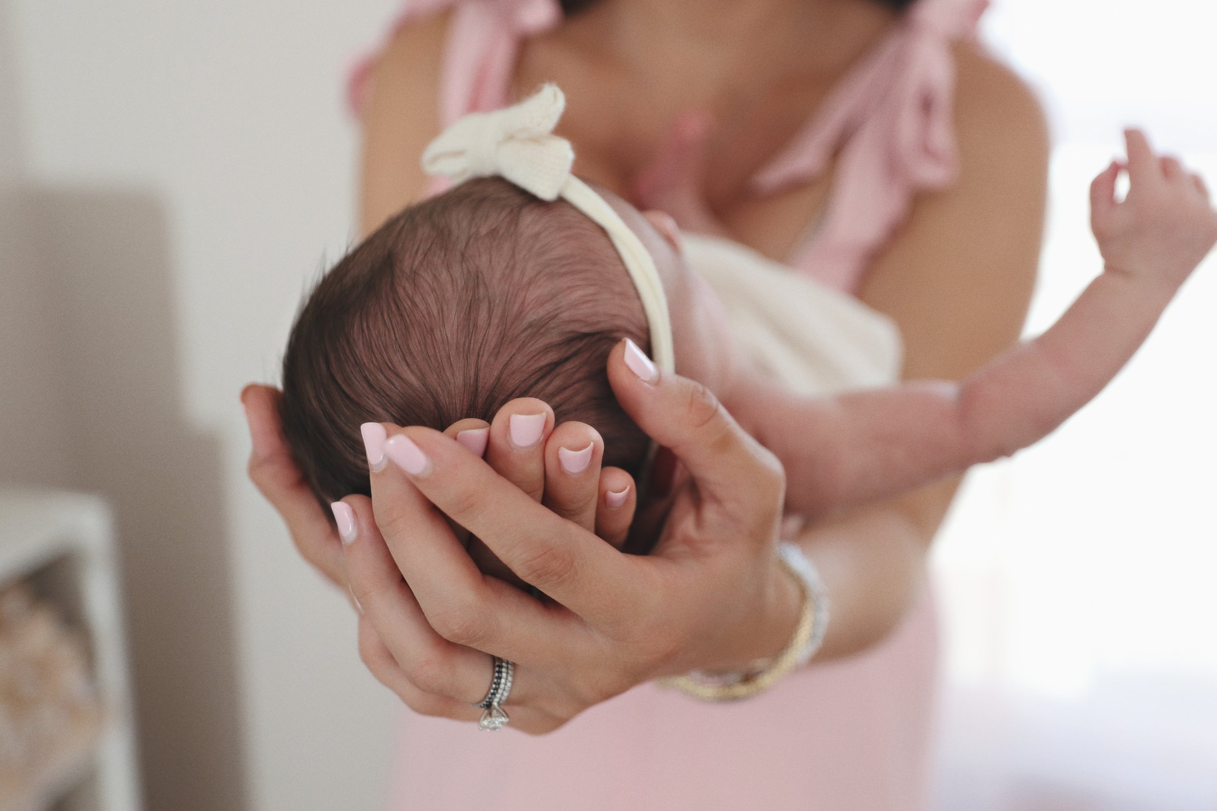 Close-up of a woman holding a sleeping newborn baby with a cream-colored headband, cradling the baby's head gently.