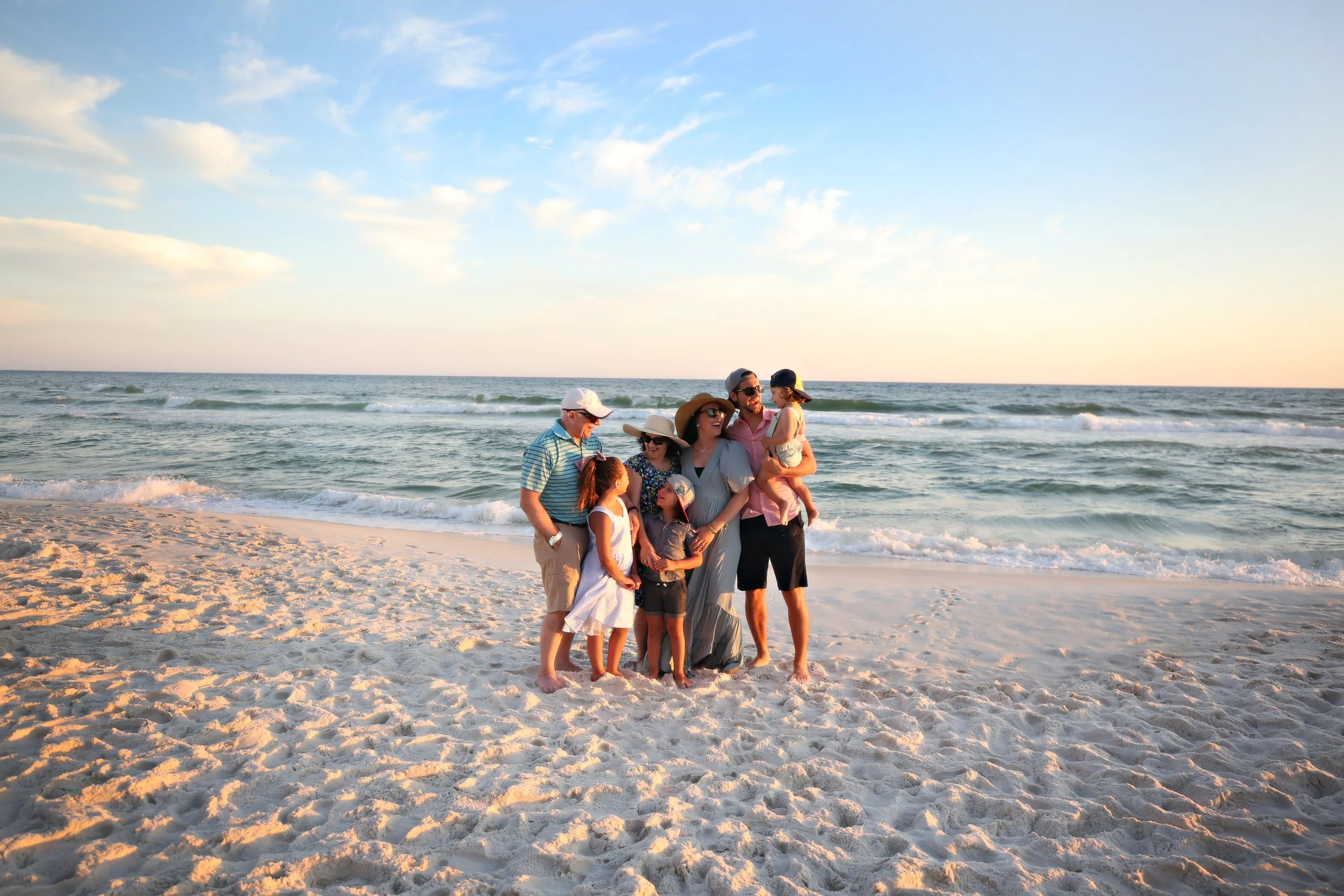 A family of six enjoying time together at the beach during sunset, standing on the sandy shore with the ocean in the background.