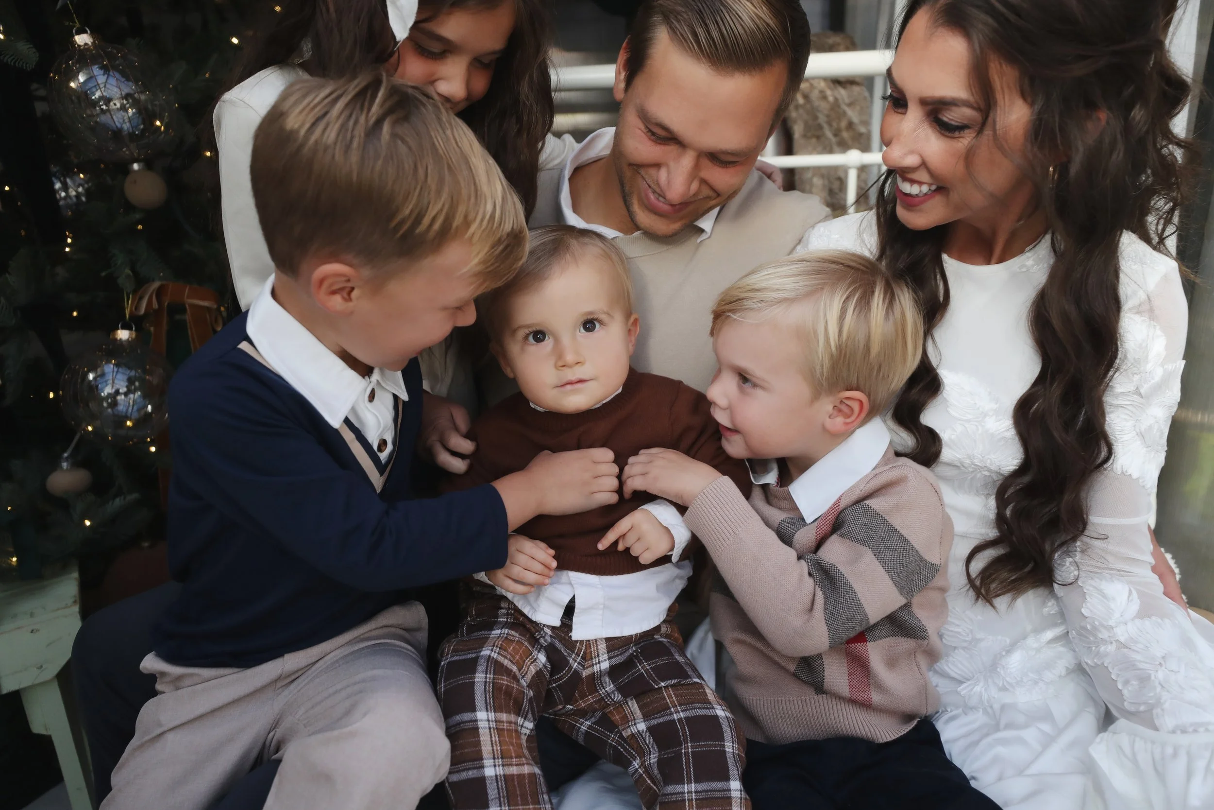 A family of seven, including adults and children, gathered together in a festive setting near a decorated Christmas tree, sharing a joyful moment.