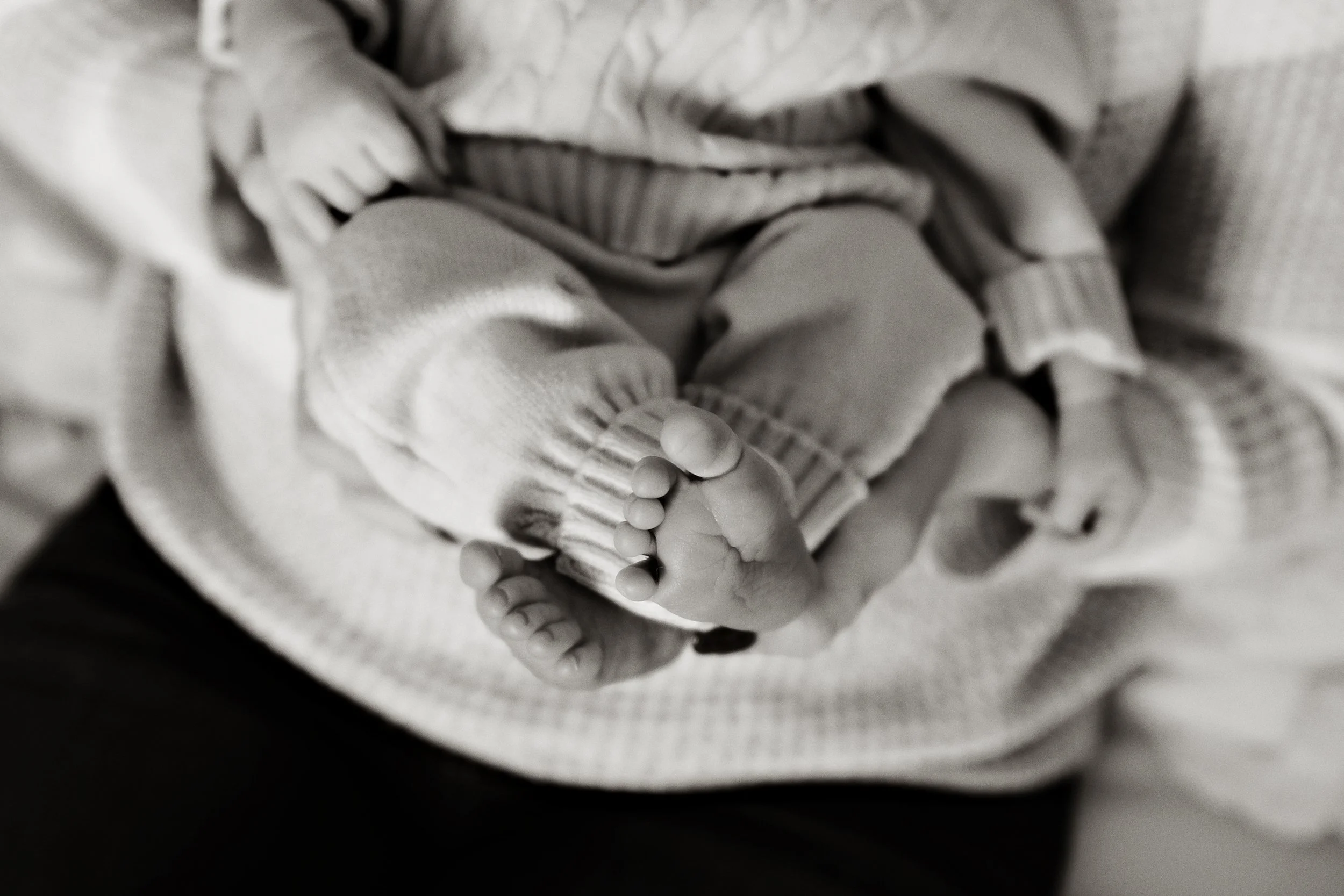 Close-up of a baby's feet, showing tiny toes, being held by an adult wearing a sweater.