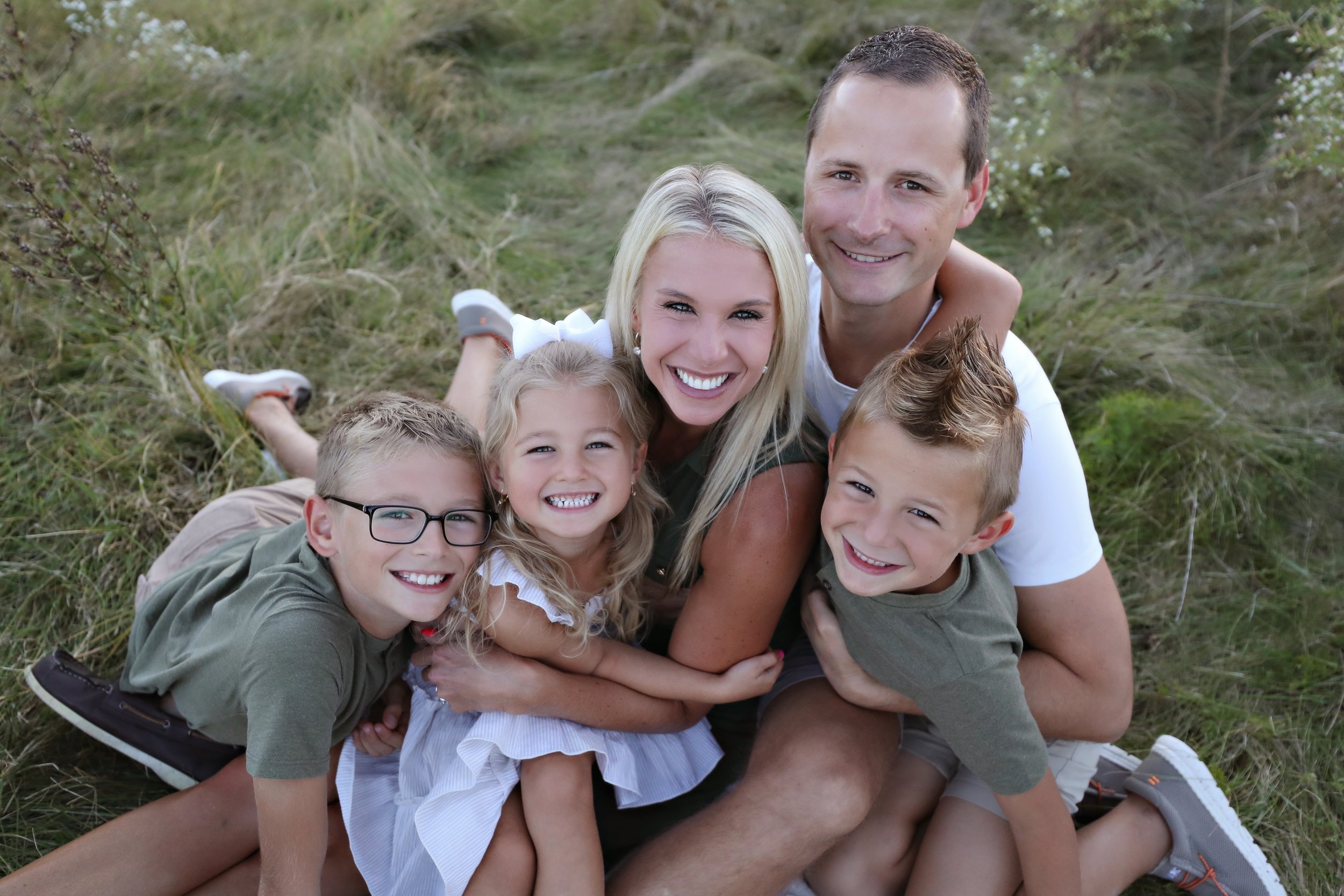A happy family of five sitting on the grass outdoors, smiling at the camera.