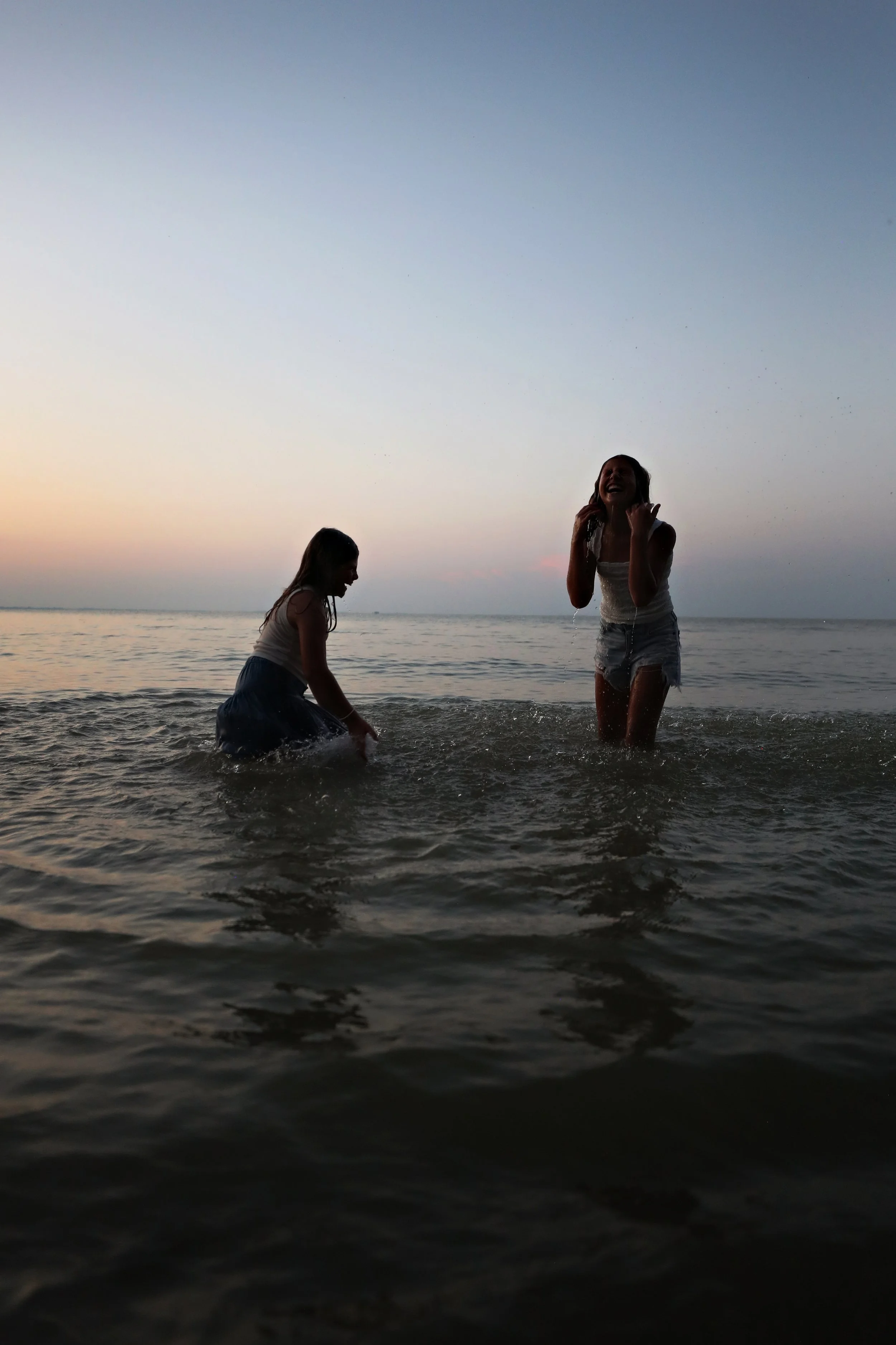 Two girls playing and splashing water in the ocean at sunset.