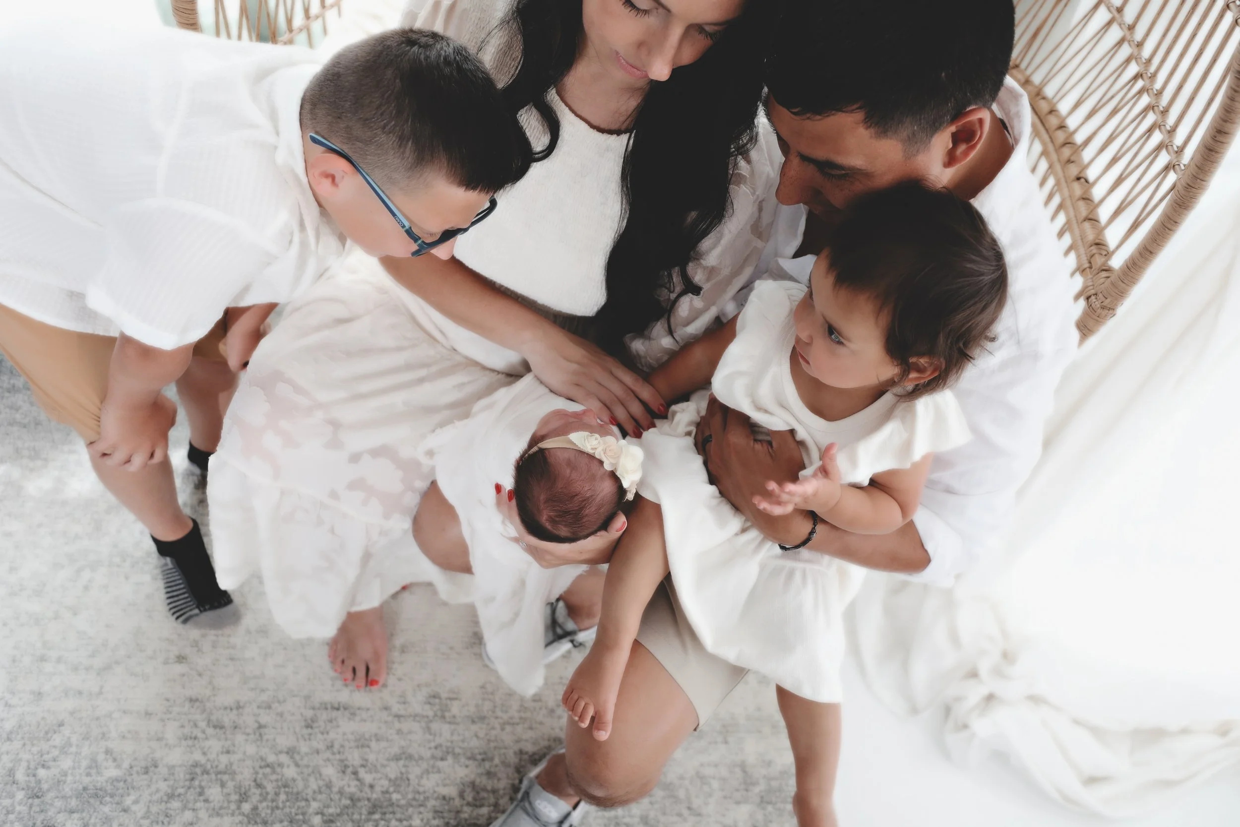 Family gathered on a bed, with infants and young children, celebrating a new baby girl.