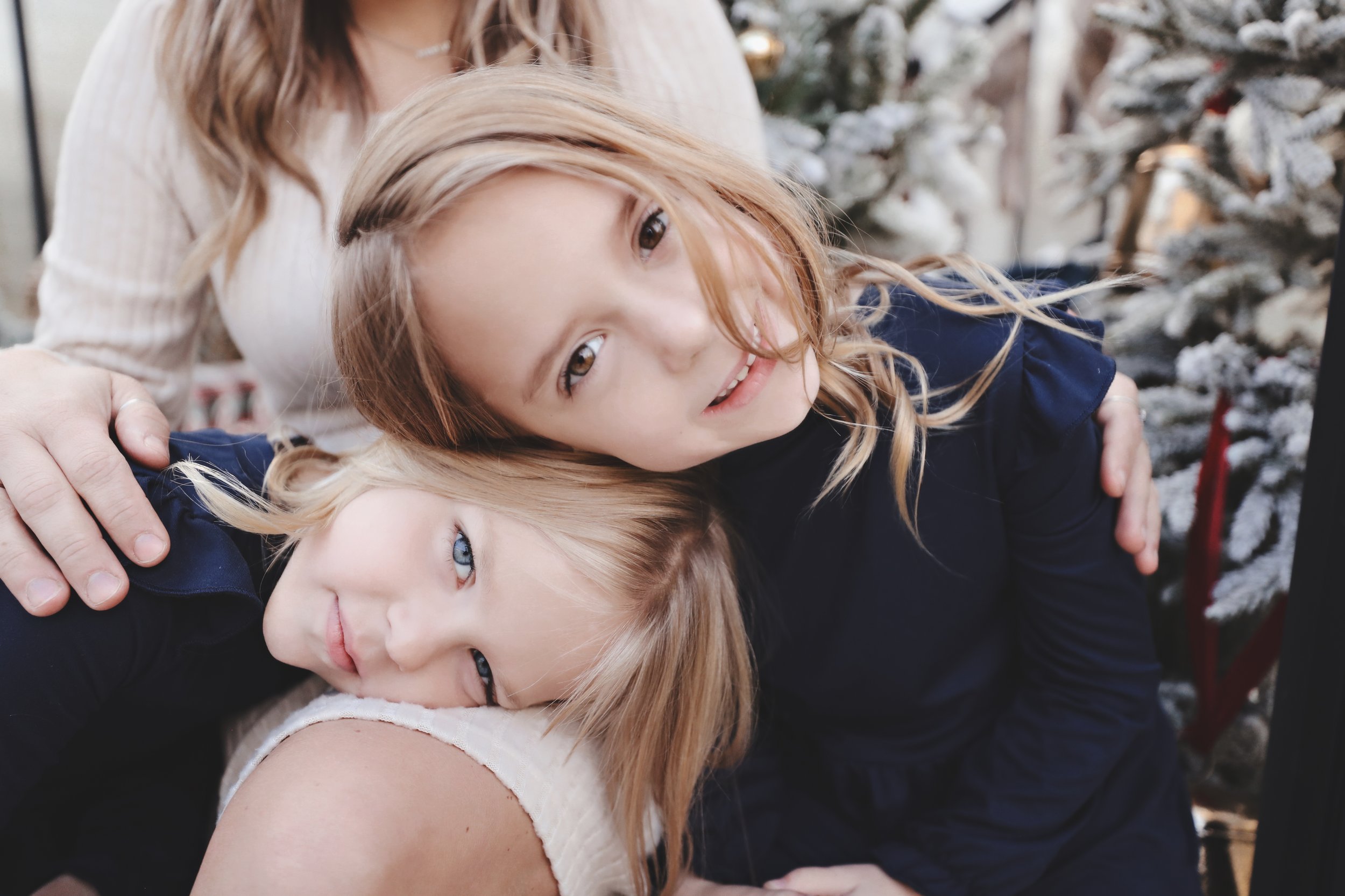 A woman with two young girls in front of a Christmas tree, all cuddling and close together.