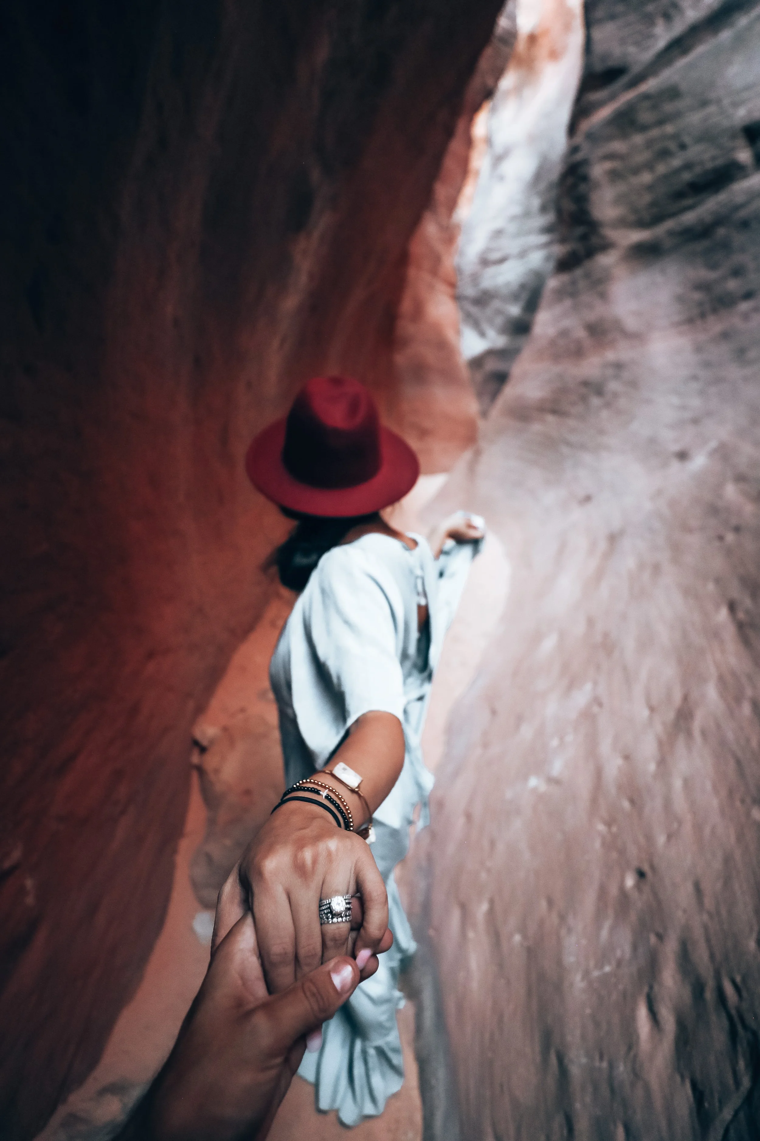 Tourists holding hands in a narrow, winding canyon with smooth, reddish rock walls.